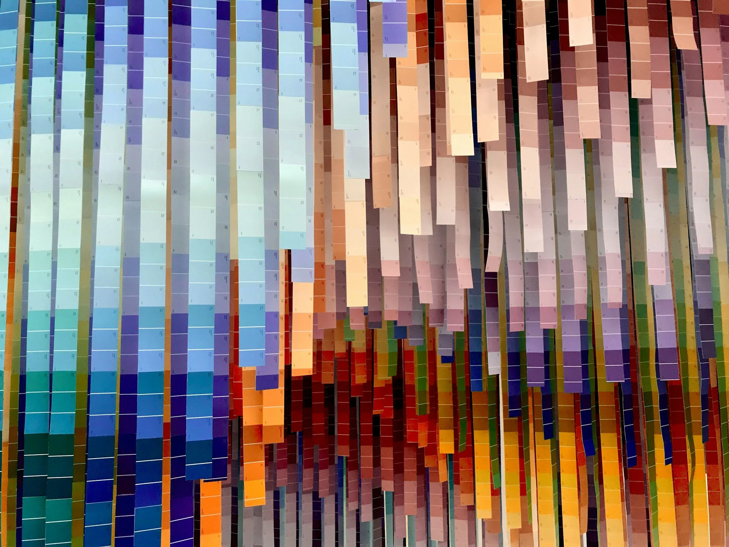 Close-up of a large color chart or palette with multiple rows and columns of small rectangular color samples, arranged in a gradient from blue on the left to red, orange, yellow, and green on the right.