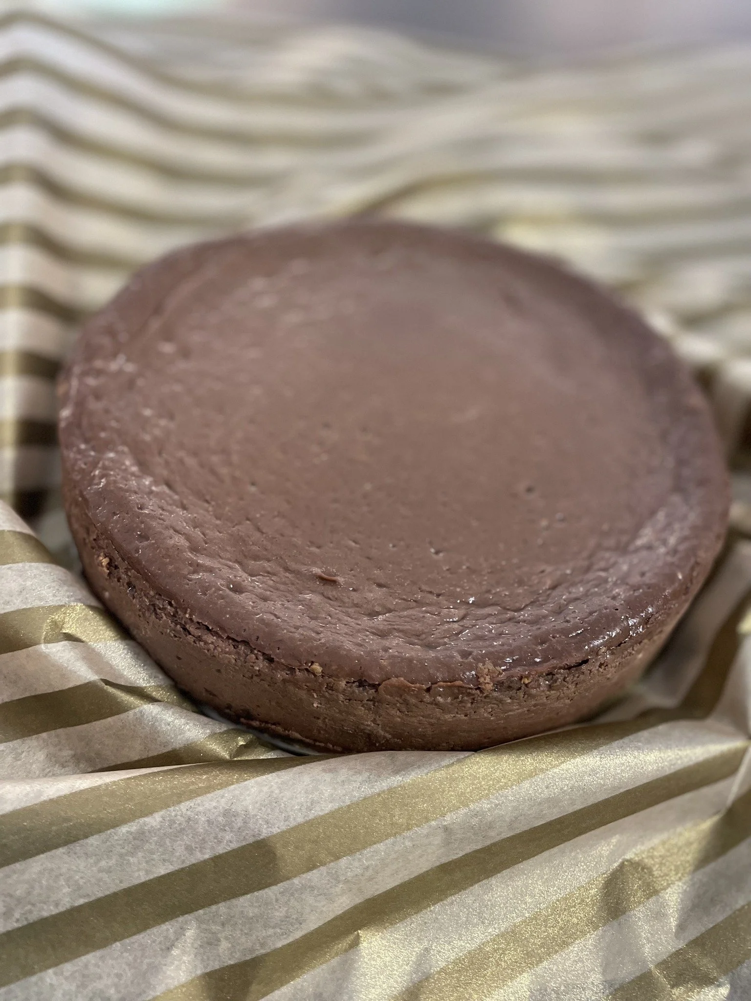 A round chocolate cheesecake, resting on a piece of gold and white striped paper or fabric.