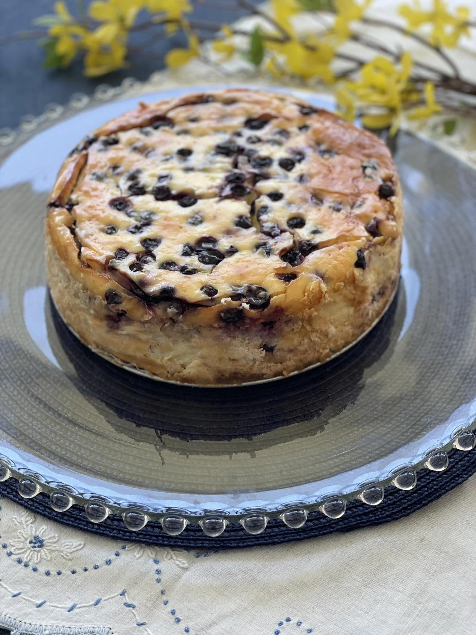 A round blueberry cheesecake on a glass cake stand