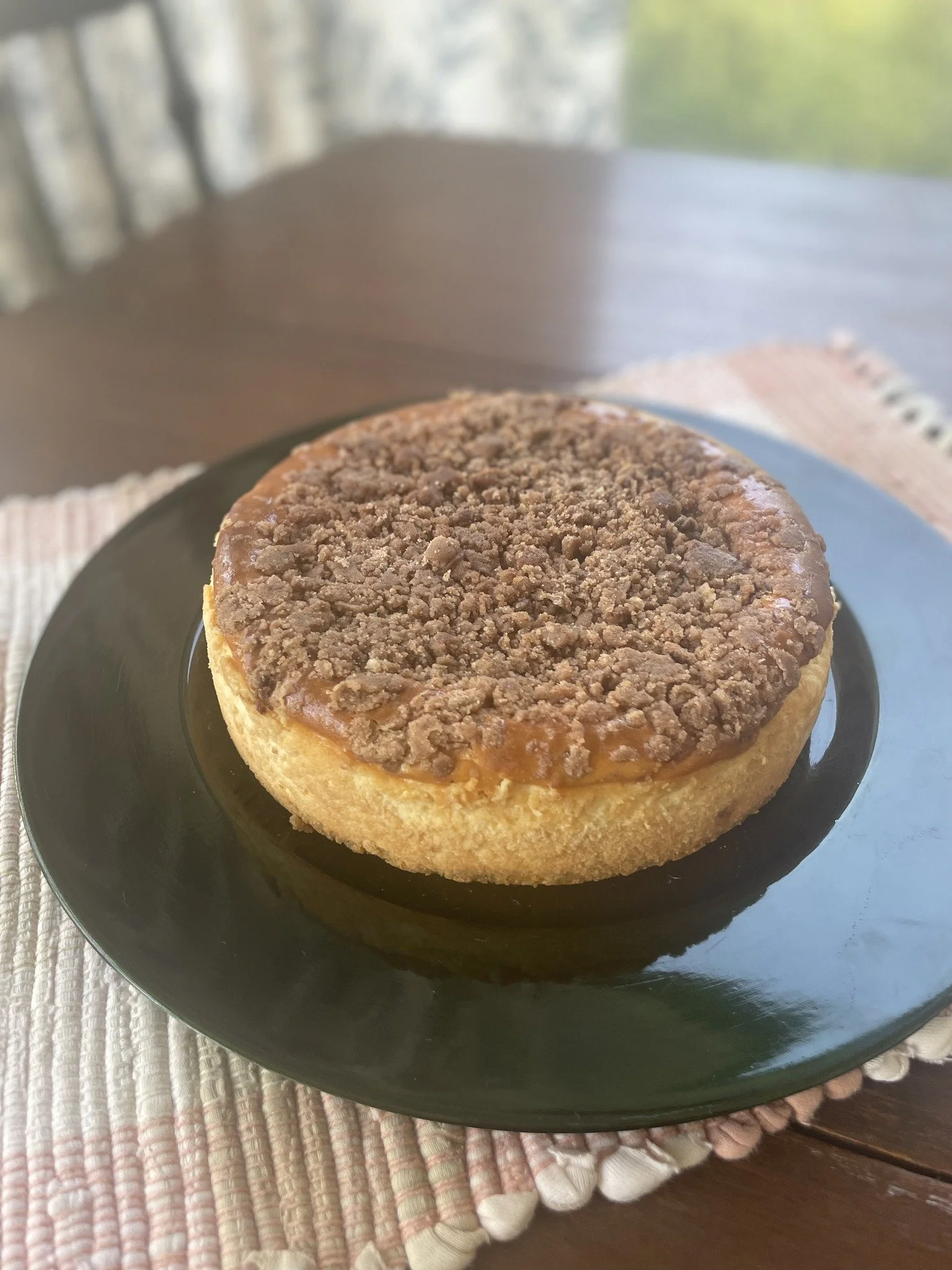 Dessert topped with crumbles on a black plate, placed on a woven placemat on a wooden table.