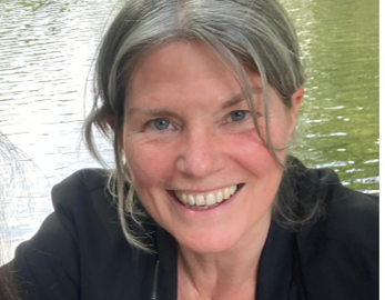 Ein Lächelndes älteres weibliches Gesicht mit grauem Haar vor Wasser im Freien.