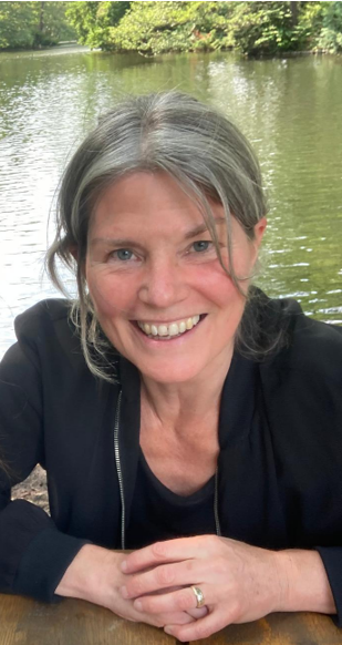 Lächelnde Frau mit grauen Haaren vor einem Fluss im Freien.