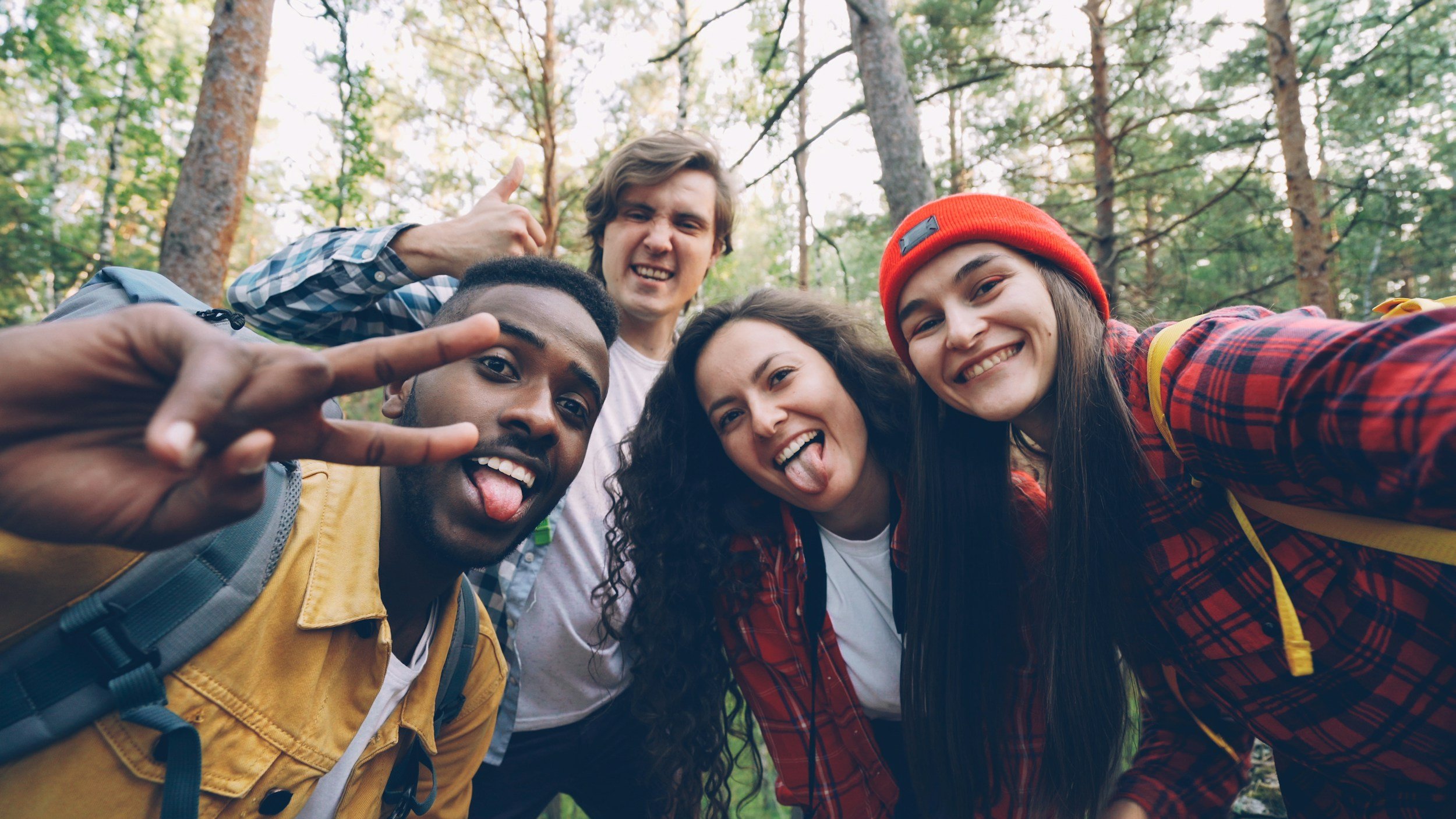 Group of five friends taking a selfie in a forest, smiling and making silly faces.