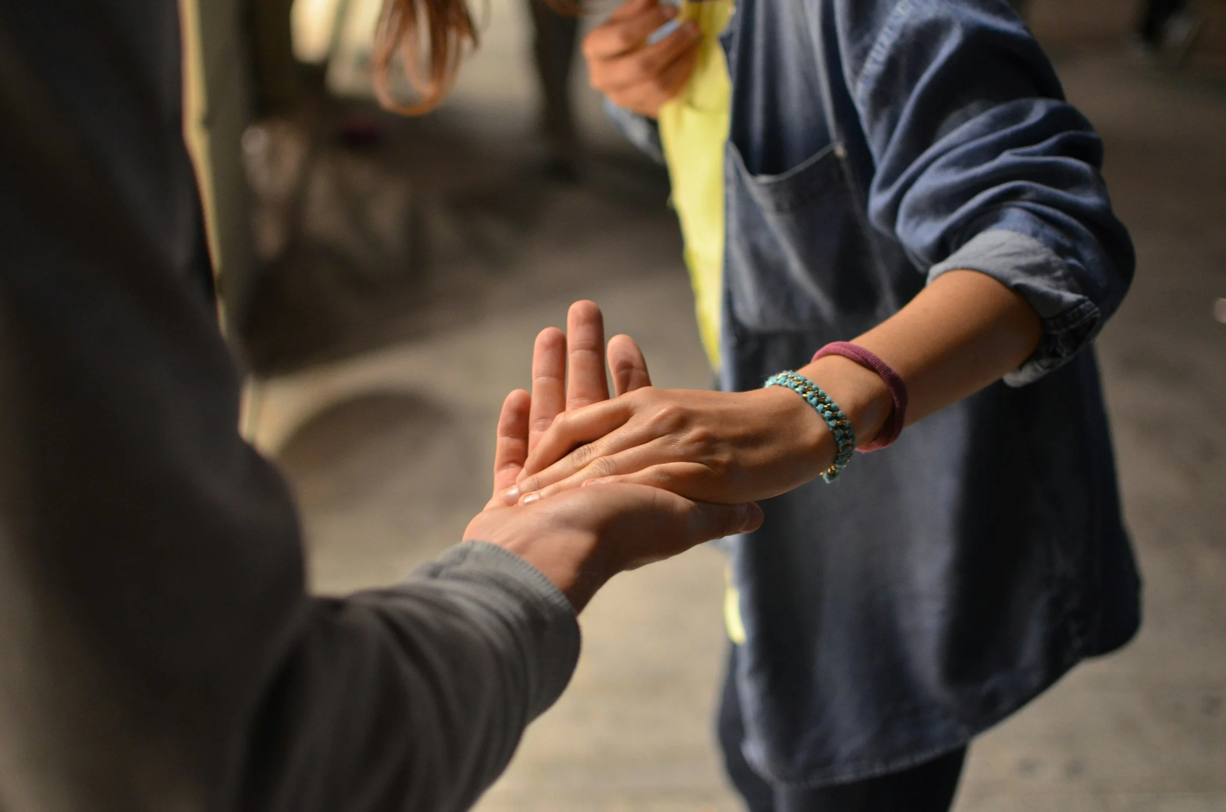 Two people holding hands, with one person's hand resting on the other's palm in a gentle gesture.