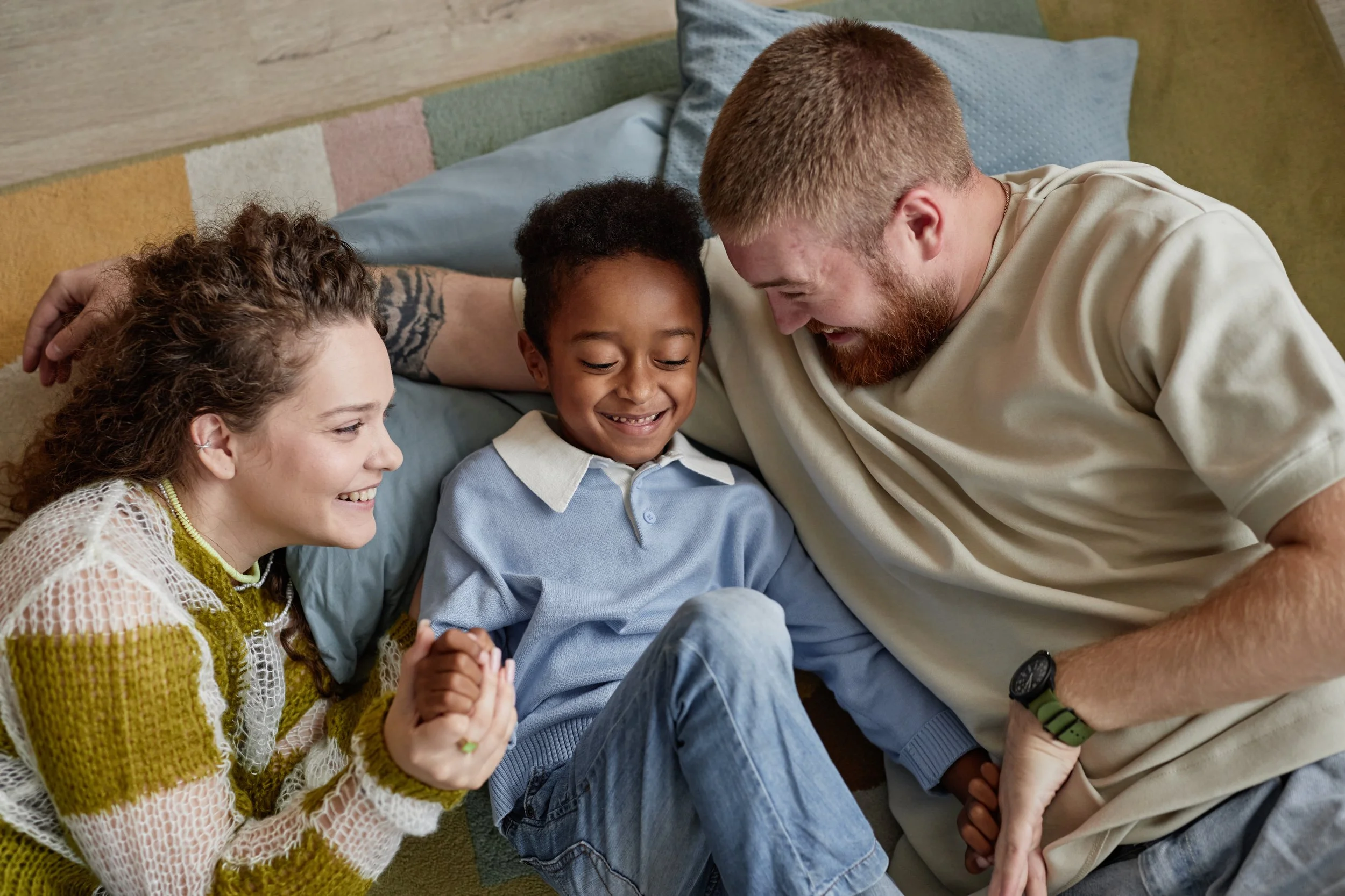 A family of three, including a young boy, his mother, and father, lying on a bed and smiling at each other.