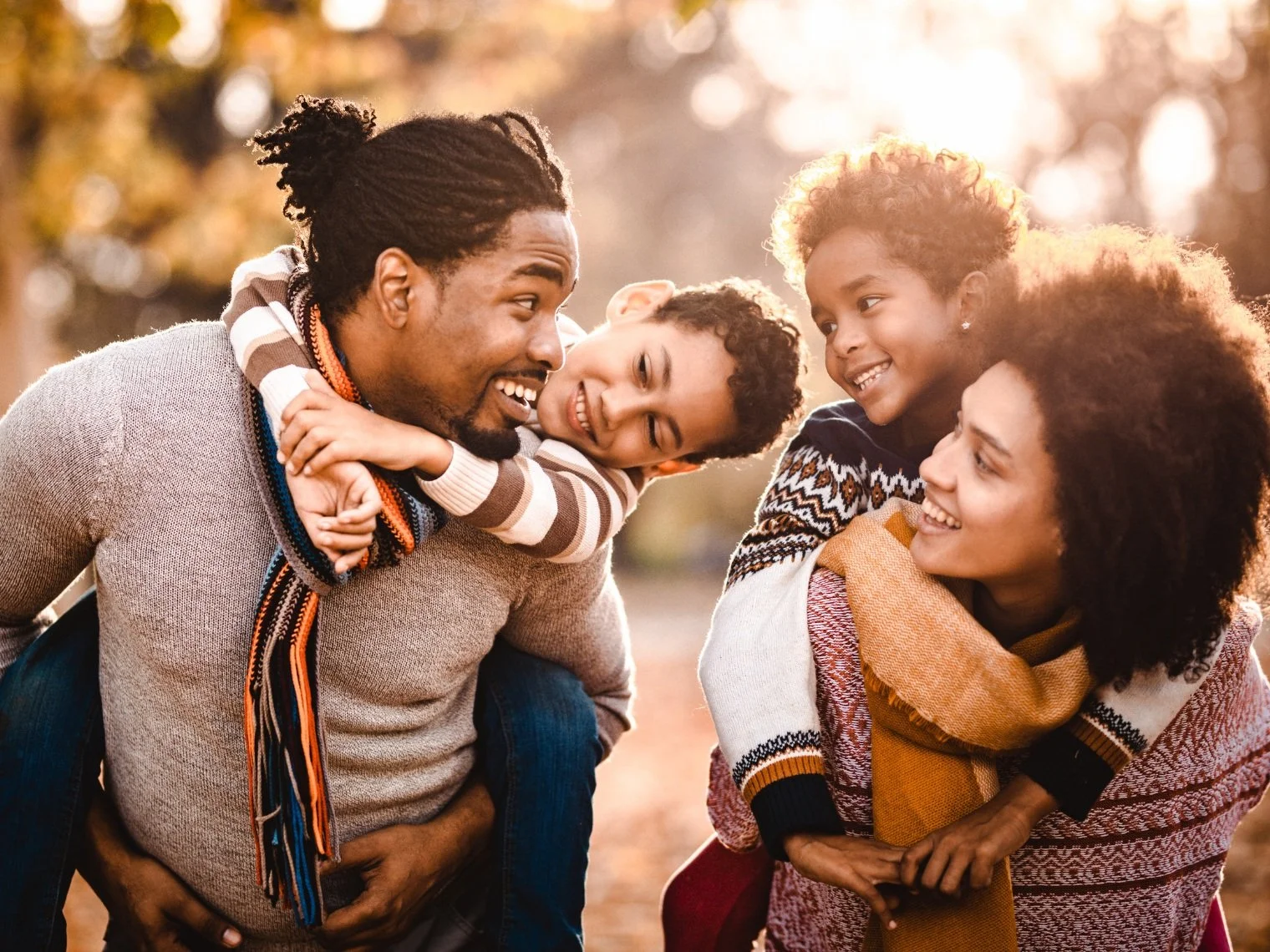 A happy family outdoors in autumn, with two fathers and two children, all smiling and engaging with each other.
