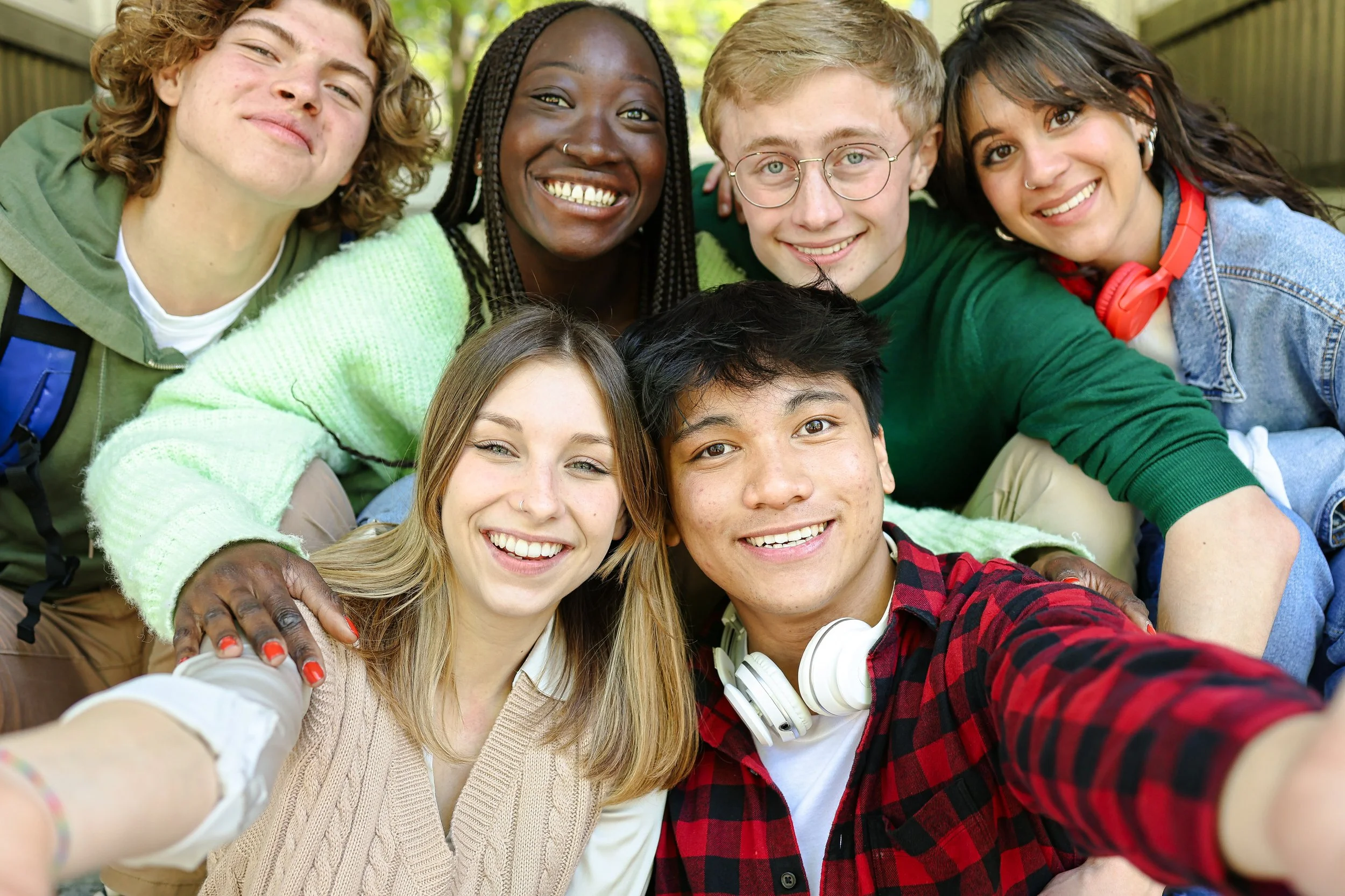 Group of seven diverse young people smiling and taking a selfie outdoors.