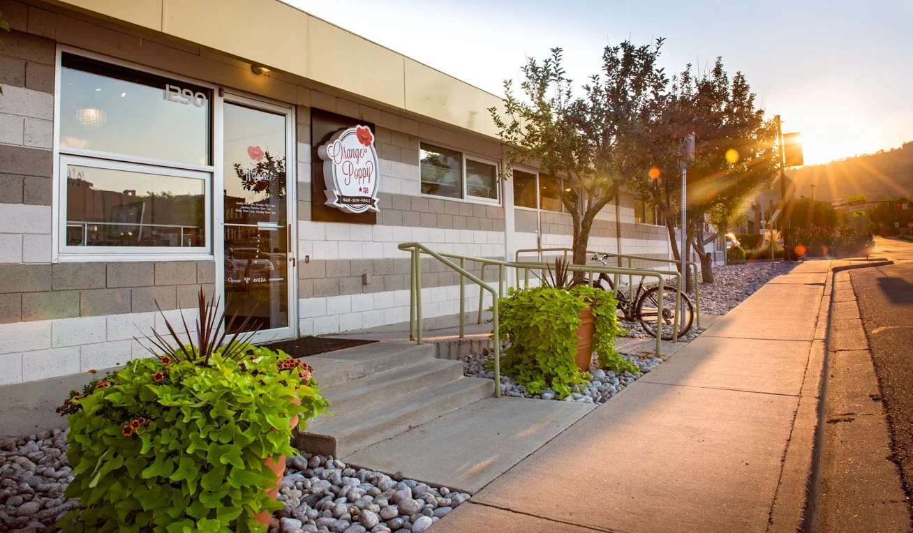 The front door of Orange Poppy Spa in Boulder, Colorado showing a ramp for access, potted flowers, and trees at sunset.