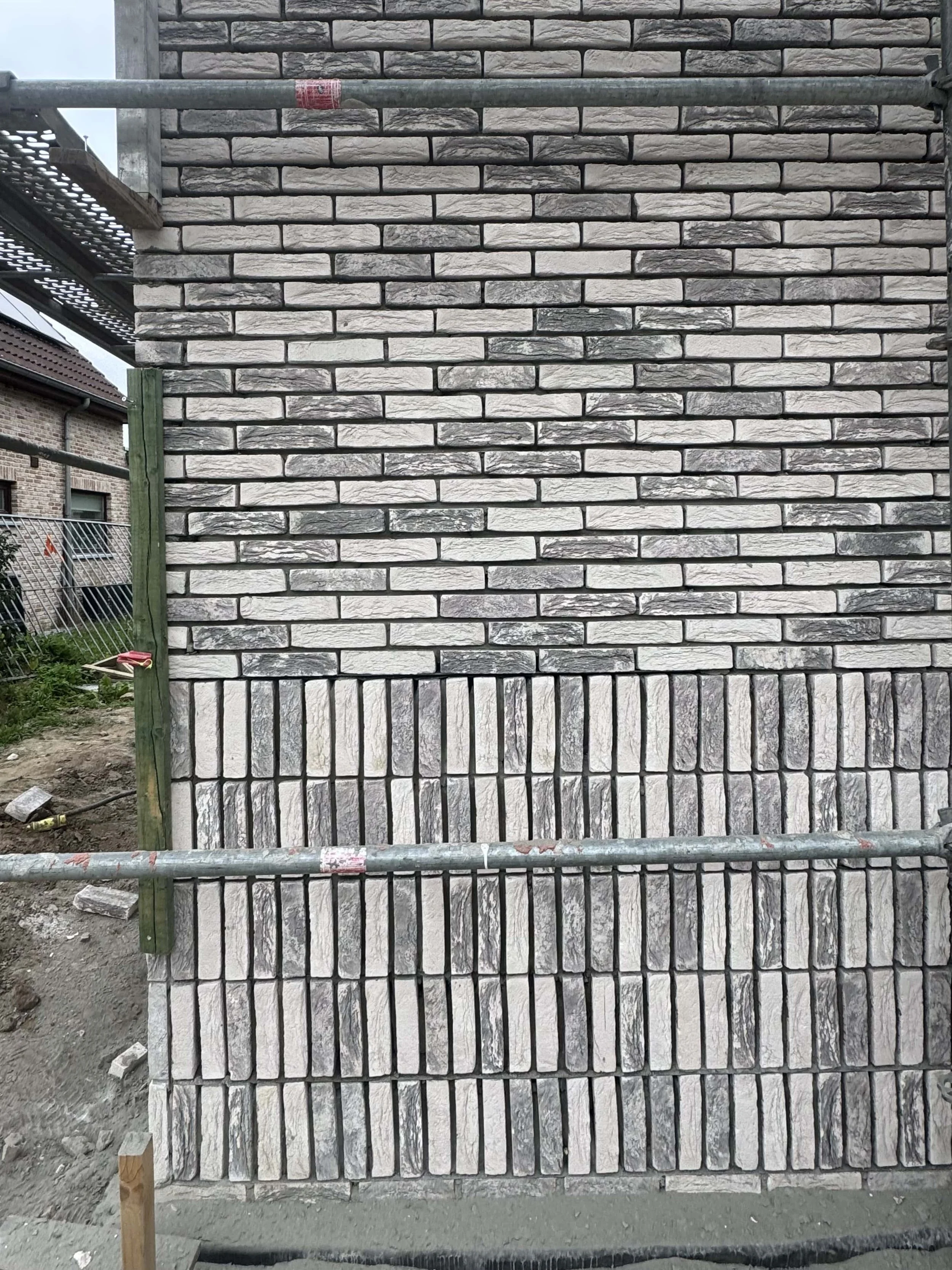 A brick wall under construction with different brick styles, partially surrounded by scaffolding at a construction site.