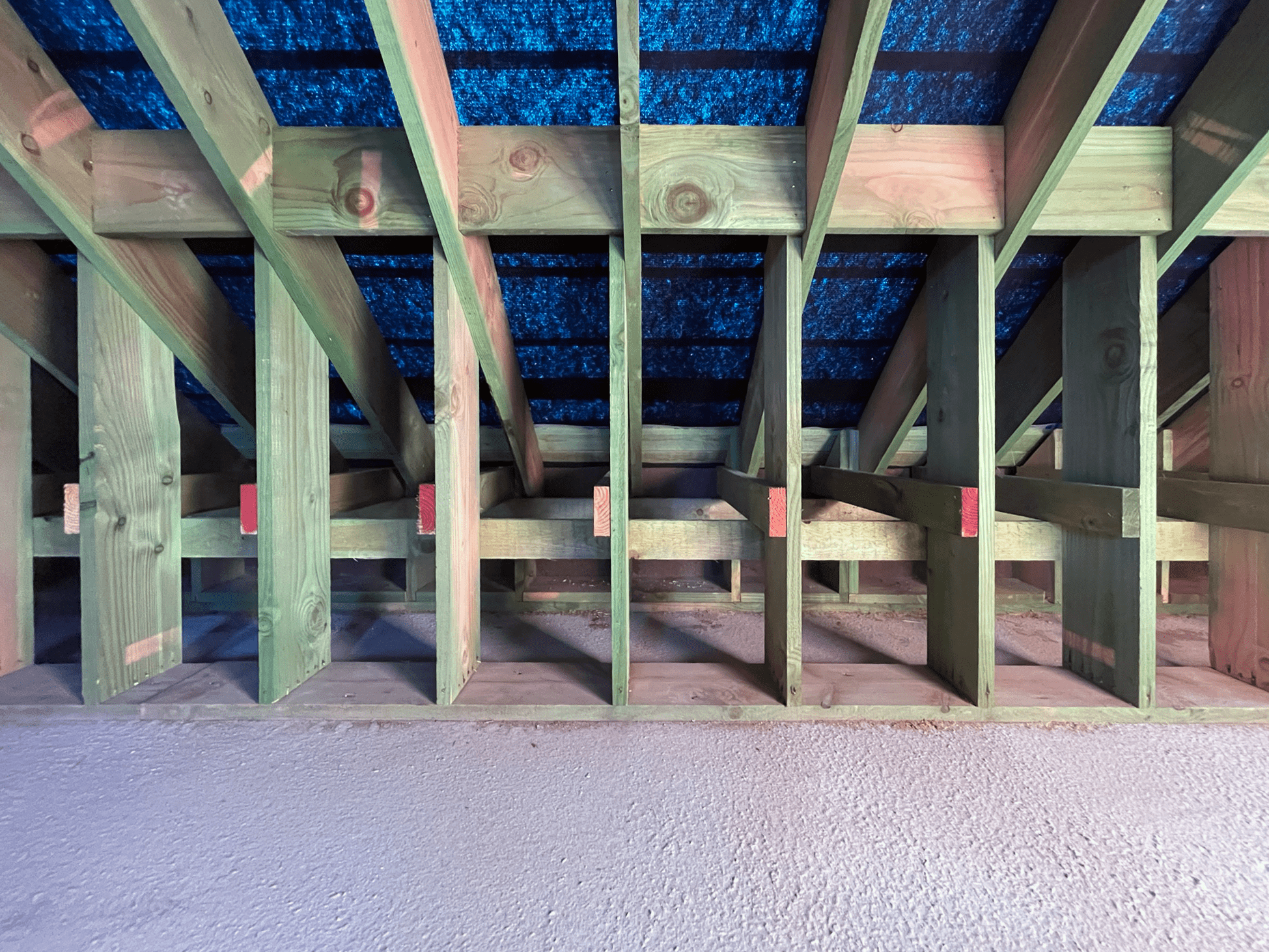 View of the underside of a wooden deck with green treated wood framing and blue roofing material underneath.