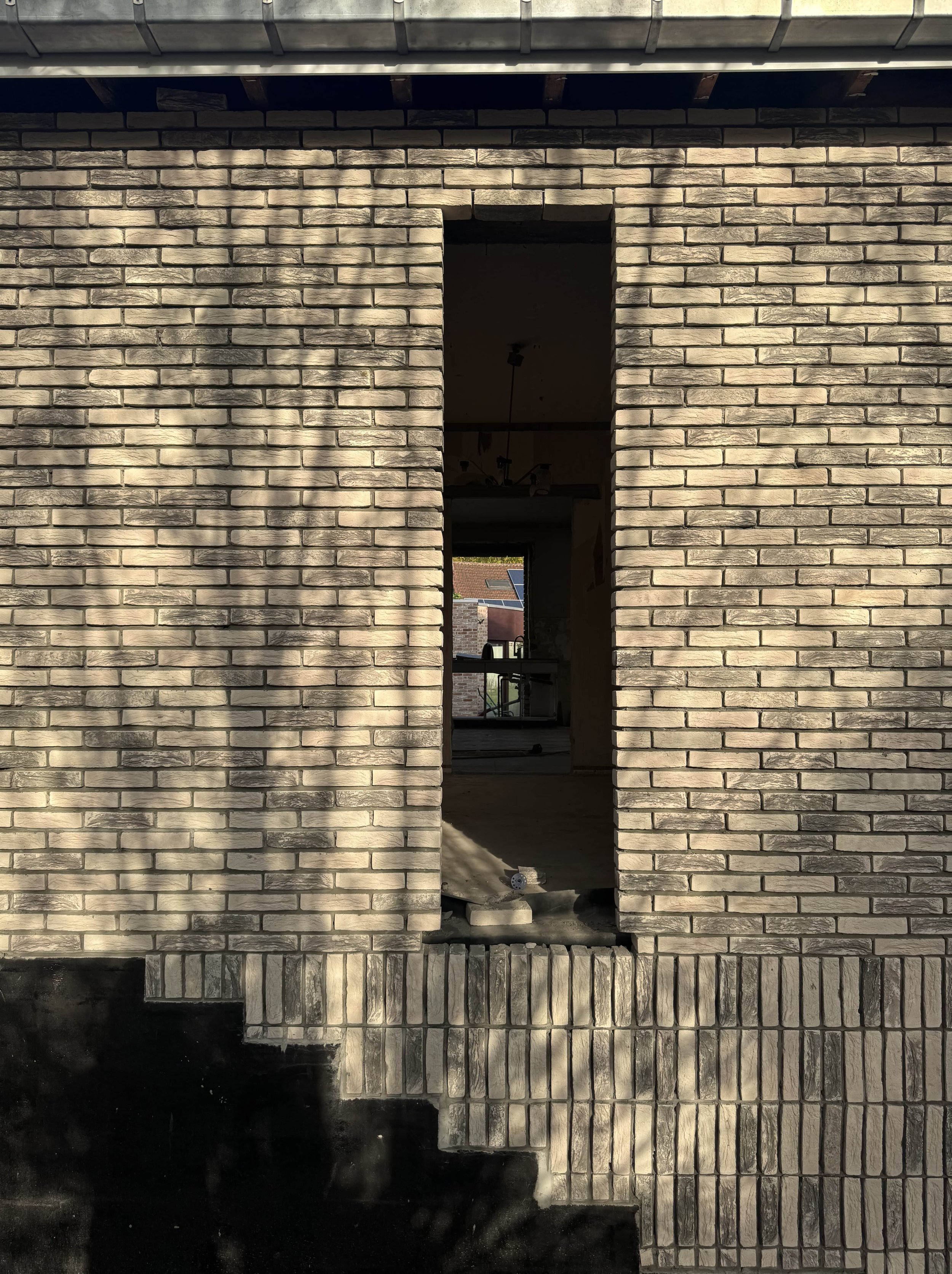A house under construction with an unfinished brick wall, open doorway, and construction materials inside.