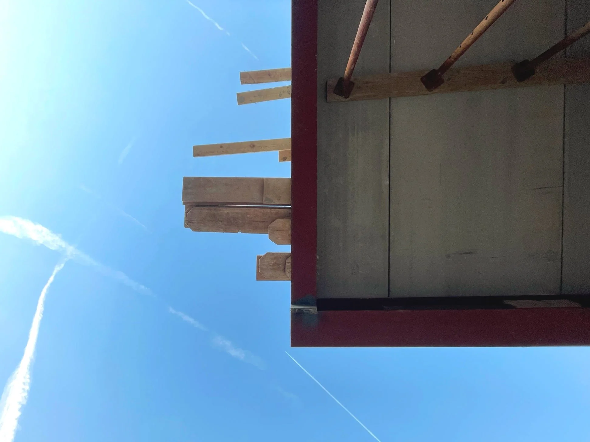 Construction site with wooden beams and tools against a blue sky with clouds and contrails.
