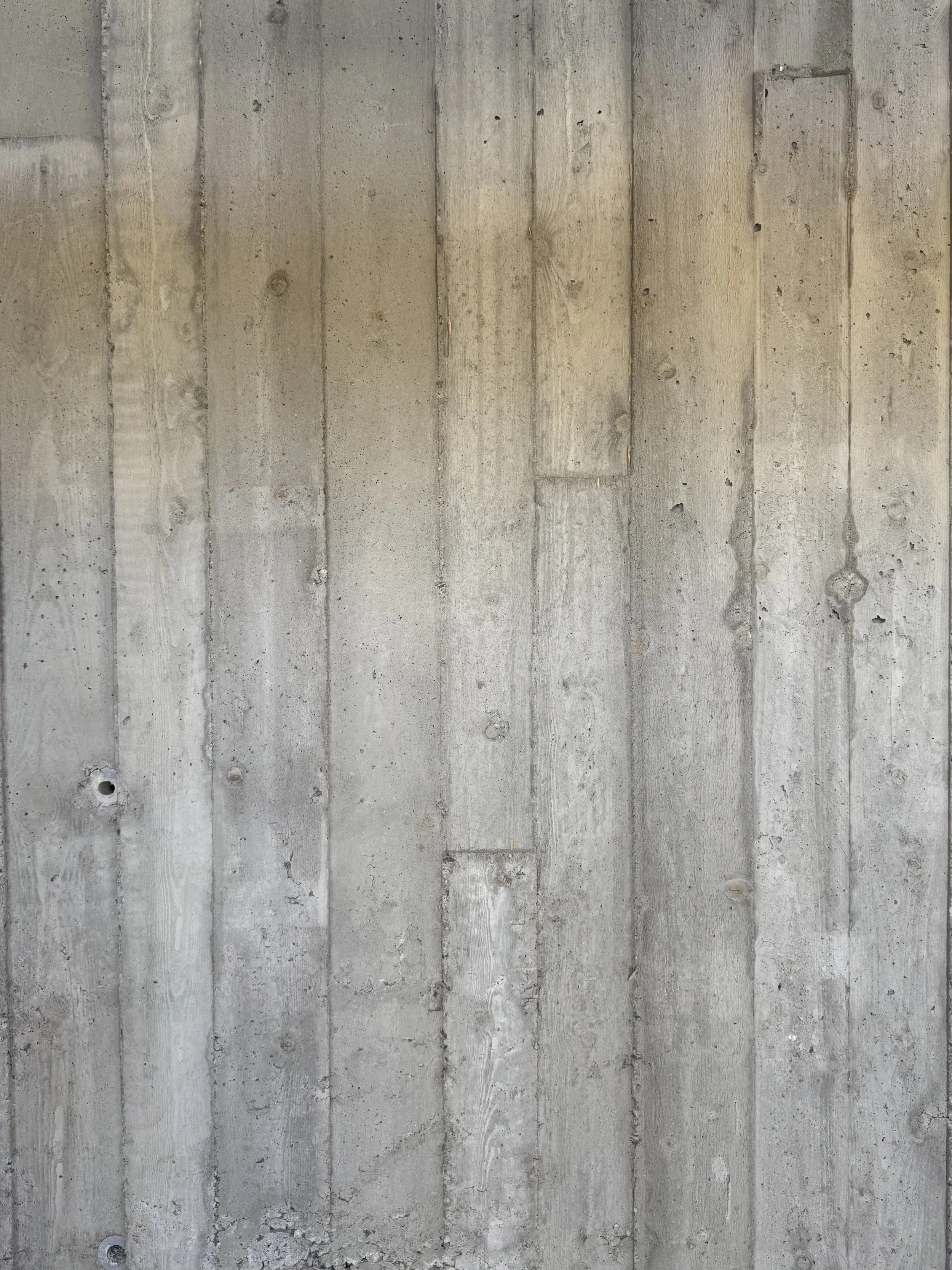 Raw concrete wall with visible vertical lines and small holes.