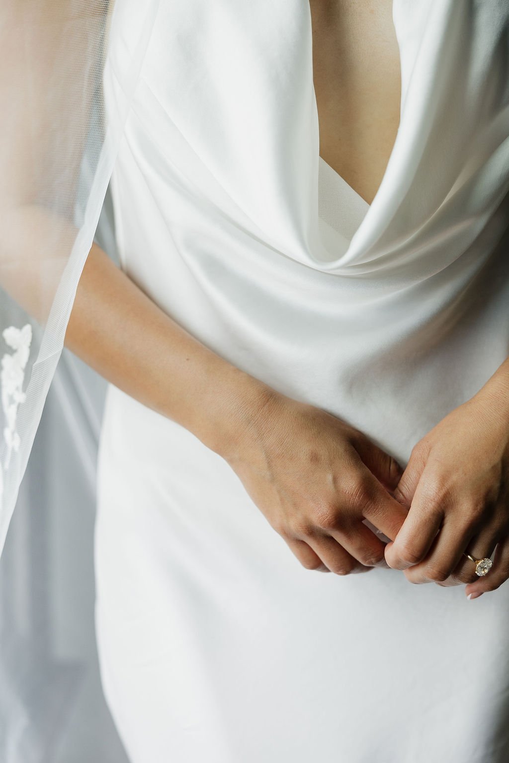 Close-up of a bride's hands holding her wedding dress, wearing a large engagement ring.