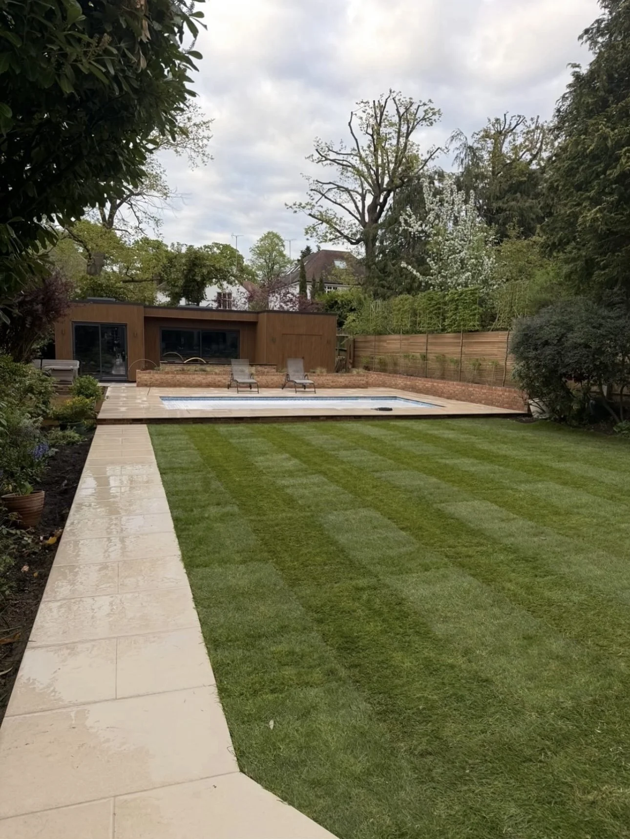 Contemporary Winchmore Hill garden with lawn, paved path, and swimming pool area