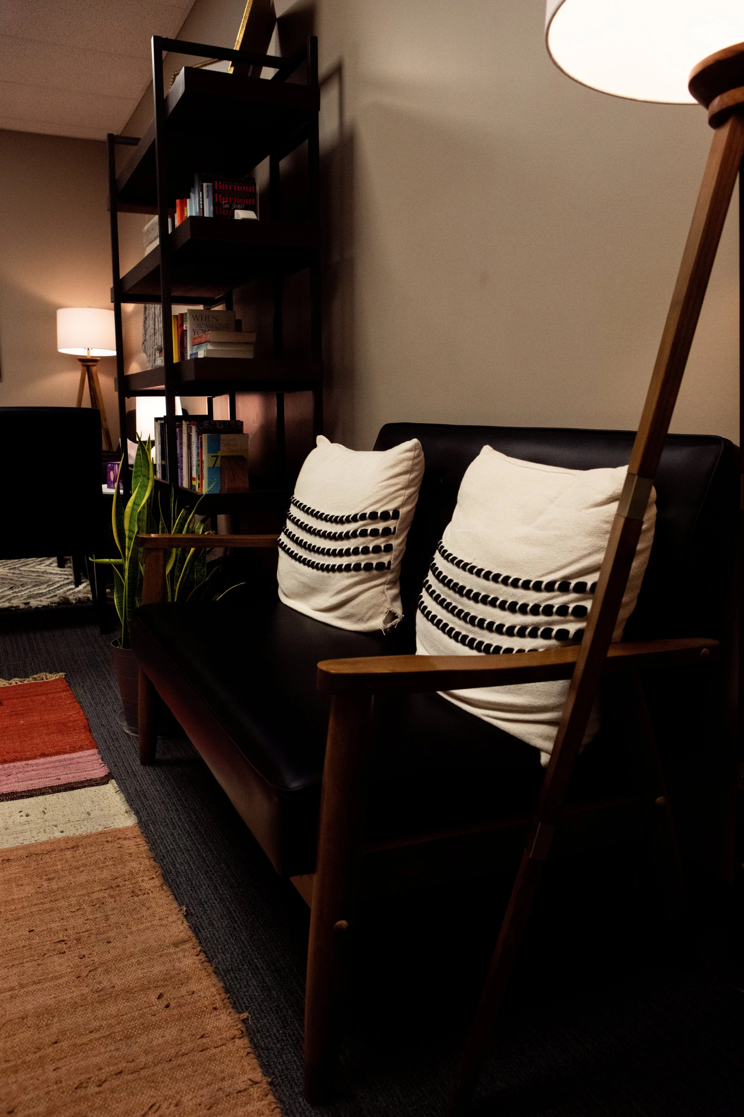 Waiting room of the Kansas City Relationship Institute. A black leather sofa and chairs, white pillows, a bookshelf with books, a potted plant, and colorful rug. Therapist Aimee Hubbard, LMFT, practices here, offering couples and individual therapy.
