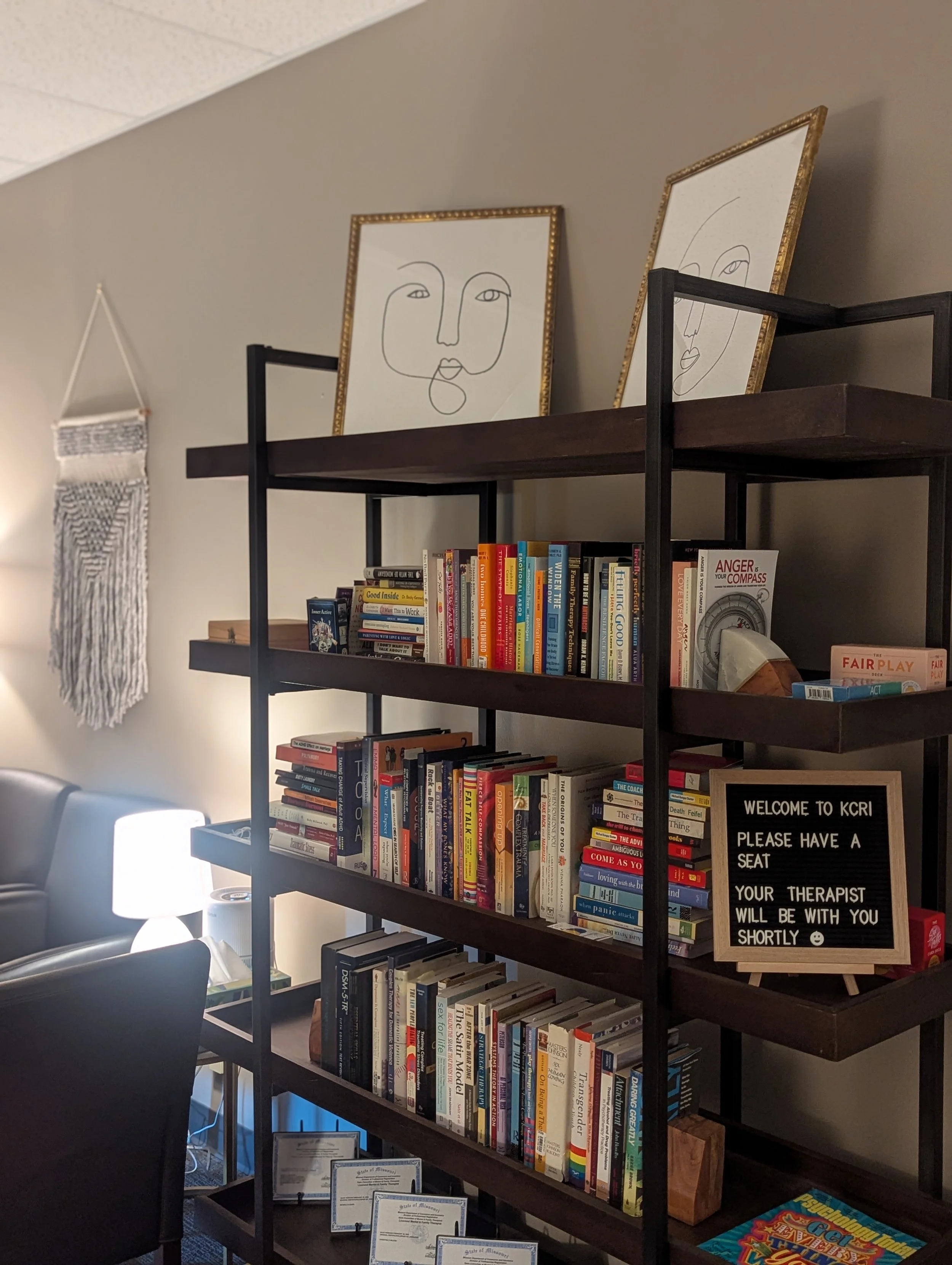 Kansas City Relationship Institute waiting room with bookshelf, black and white paintings above the bookshelf help to create a welcoming environment for therapy clients.
