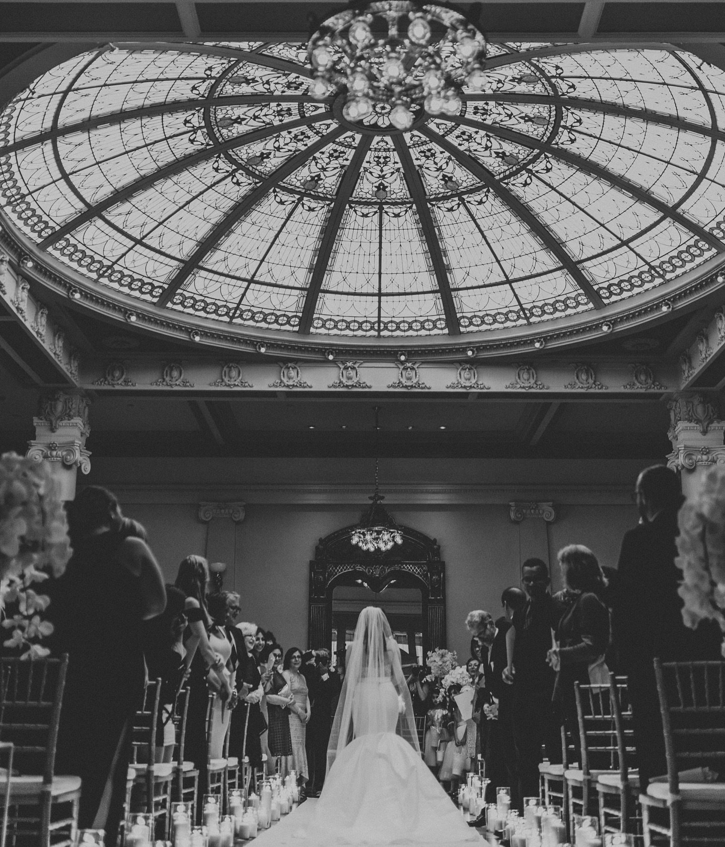 A setting that spoke volumes.
Candles illuminating the aisle, a ceiling that stole hearts, and a bride that completed the scene.

Every element of this moment was designed to feel timeless. The glow of candlelight reflected softly across the room, gu