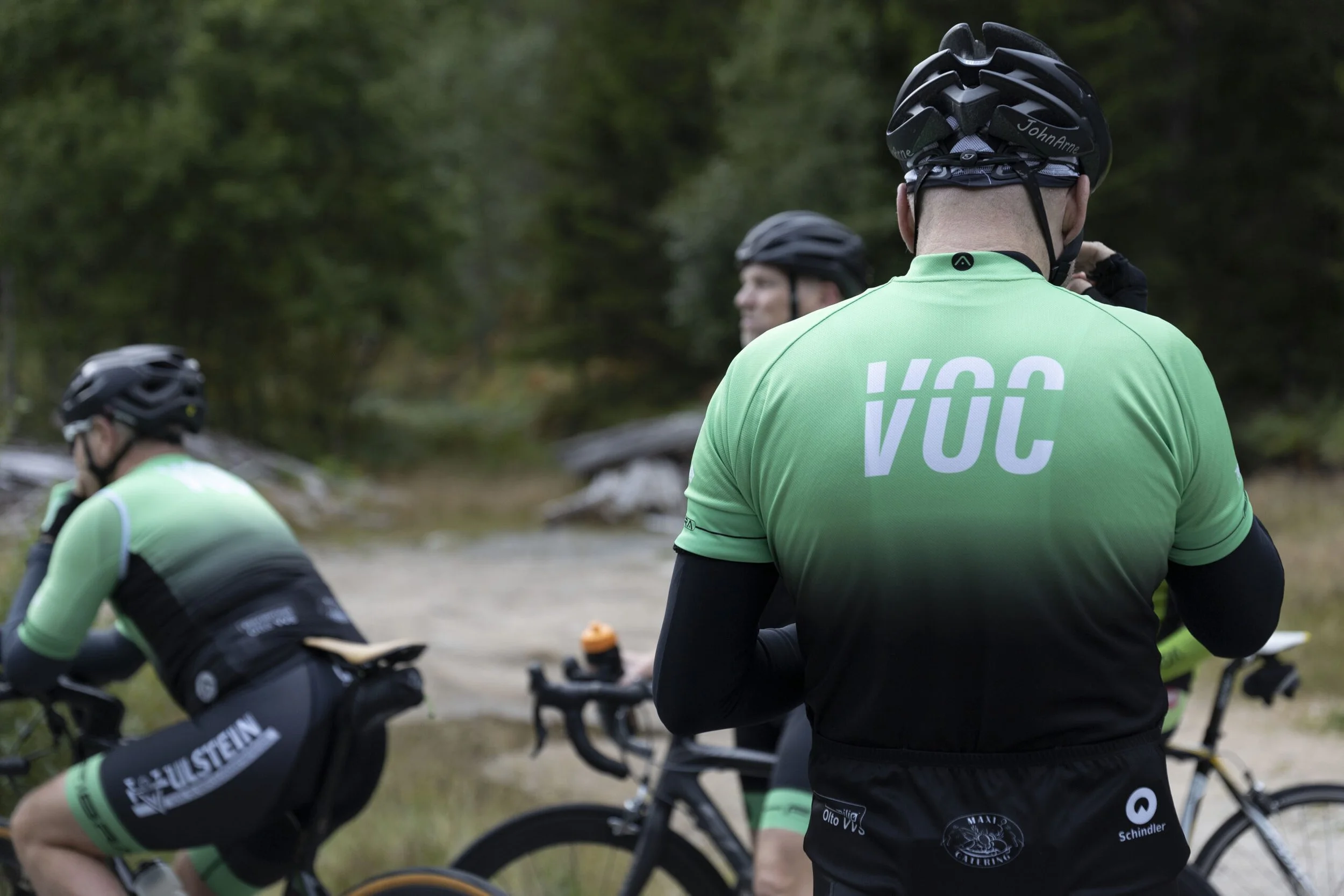 Tre syklister i matchende grønne og svarte sykler og hjelmer på en syklingetur i skogen.