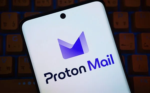 A smartphone sitting on a loptop keyboard displaying the Proton Mail Logo on a white background.