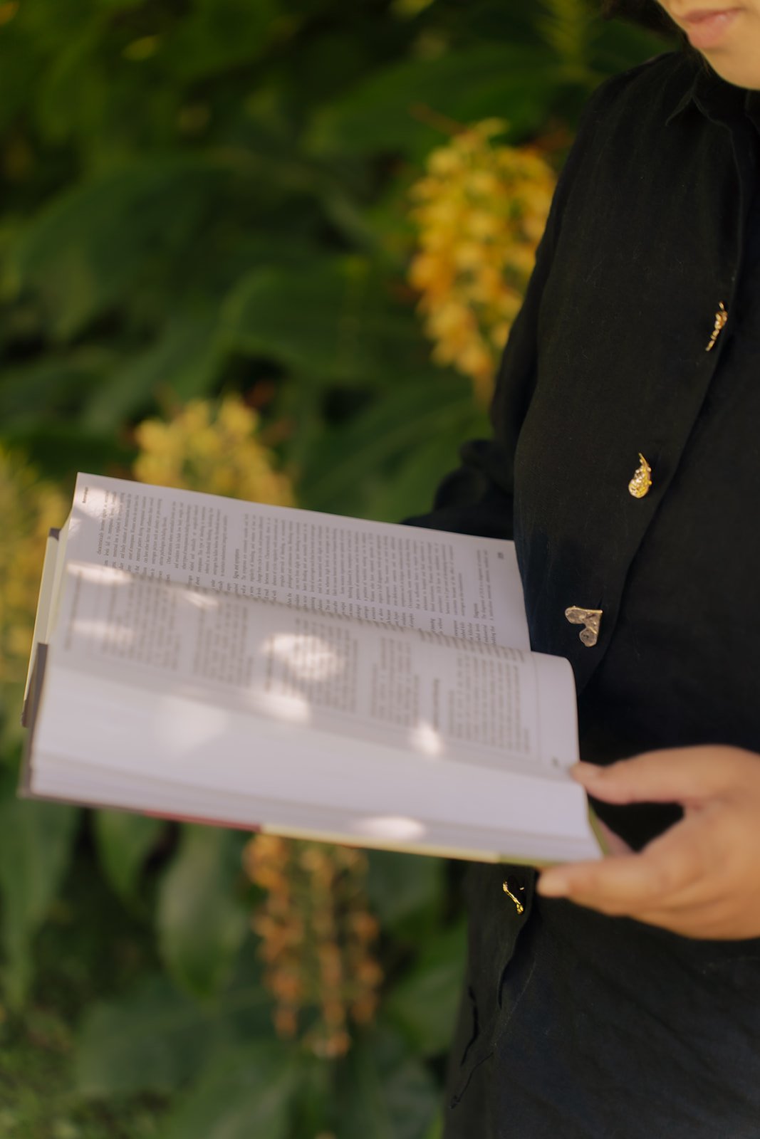 Person reading a book outdoors near green foliage