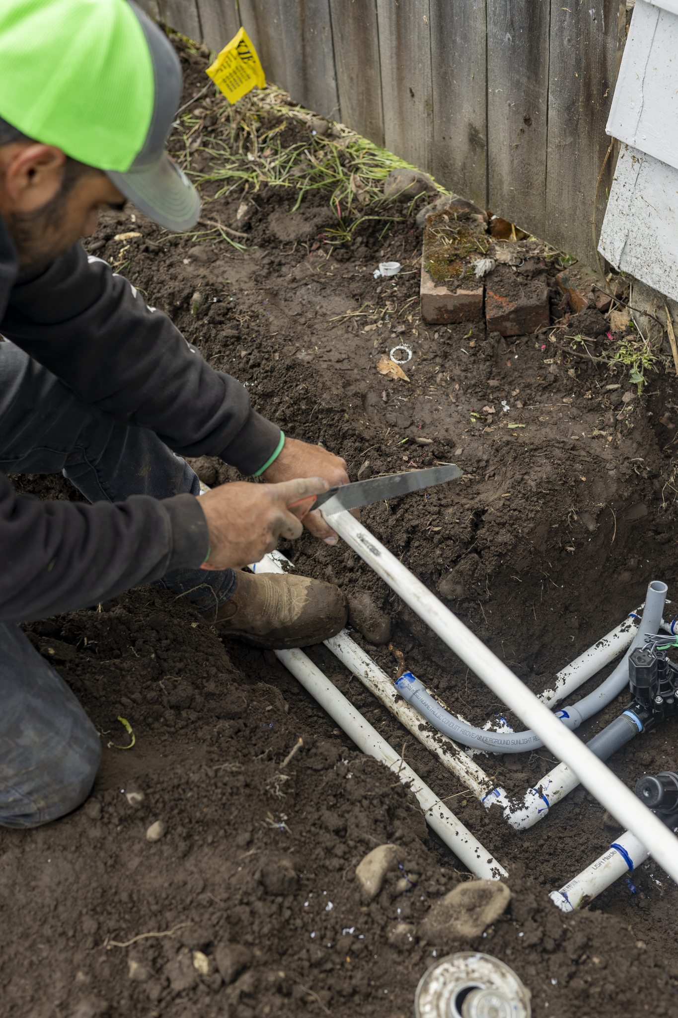 A person working on installing plumbing underground, with white PVC pipes and dirt.