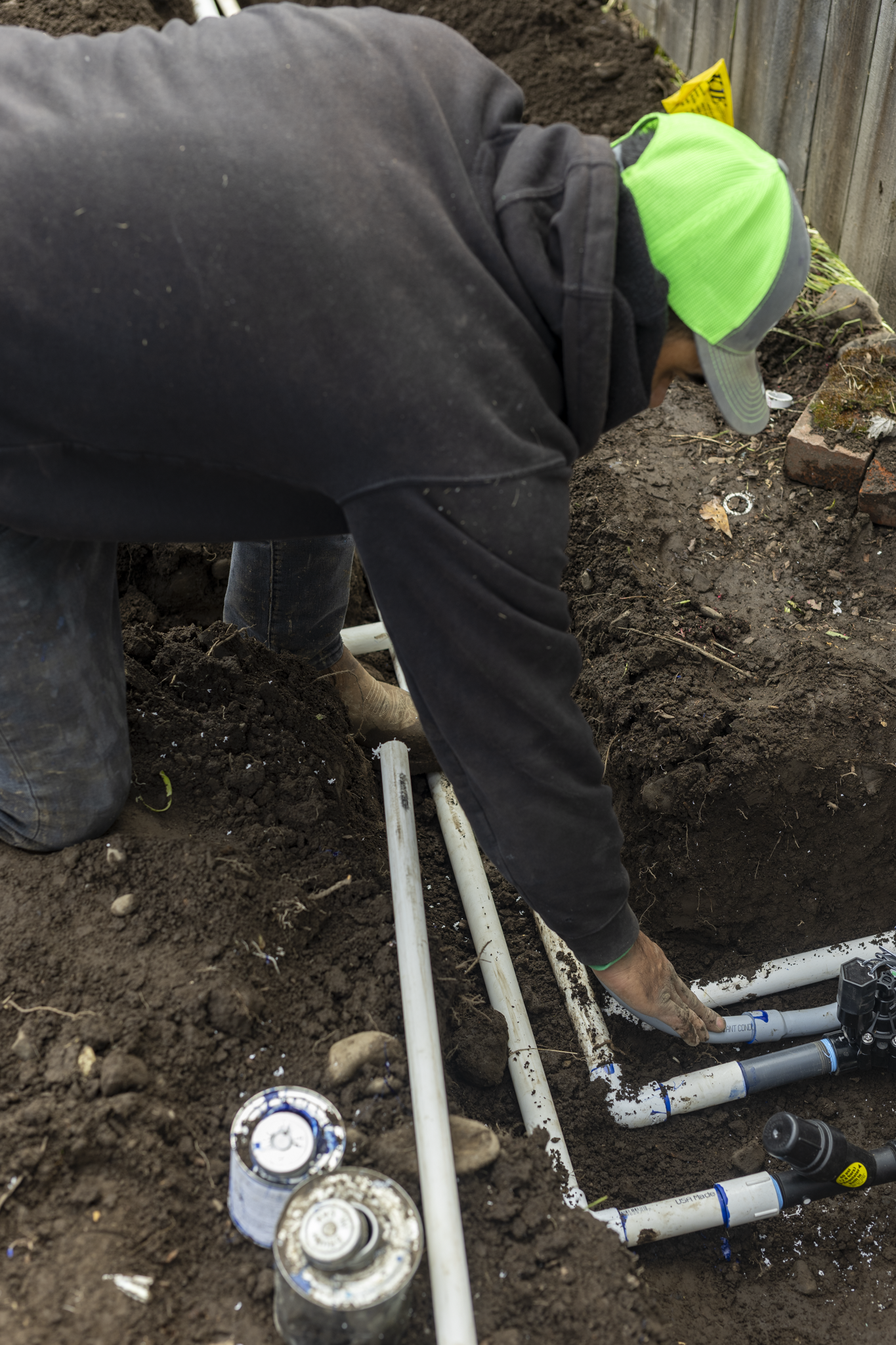 A person working on plumbing in a garden or backyard, installing PVC pipes underground.