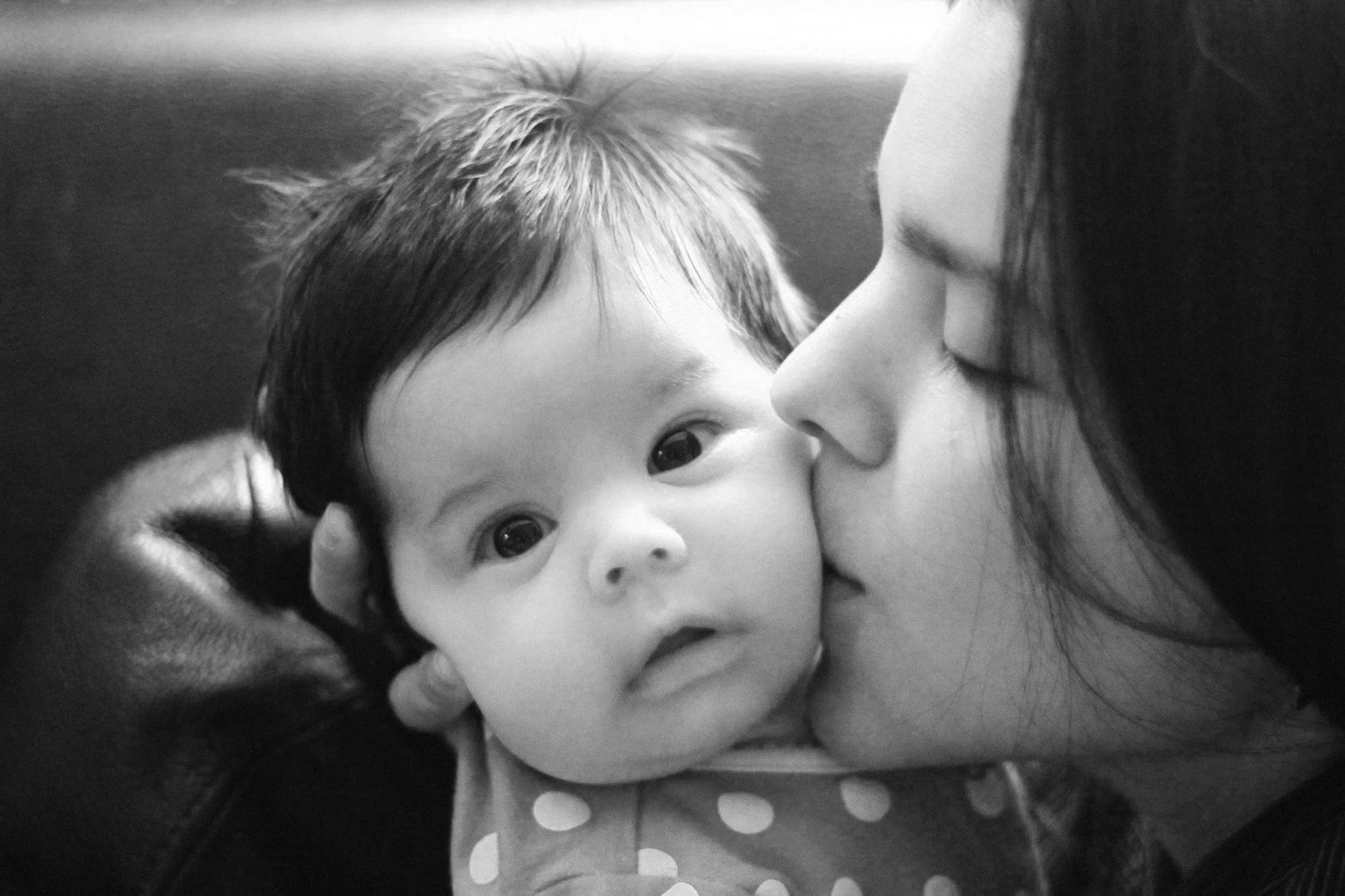 Close-up of a mother gently kissing her baby’s cheek, representing connection, emotional attunement, and the sensitive bond in early parenthood.