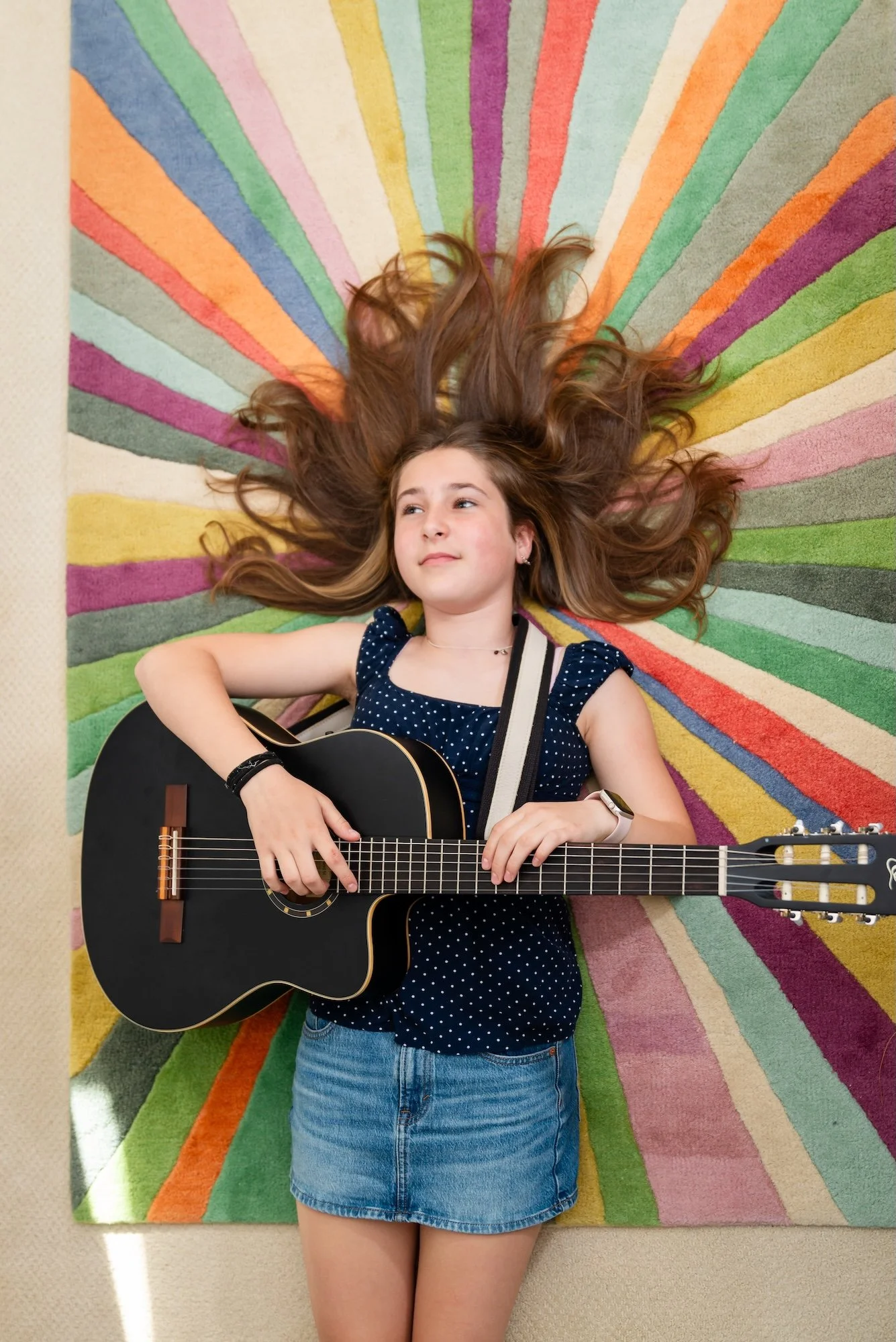 Pre-teen girl with long brown hair playing an acoustic guitar on a striped rug