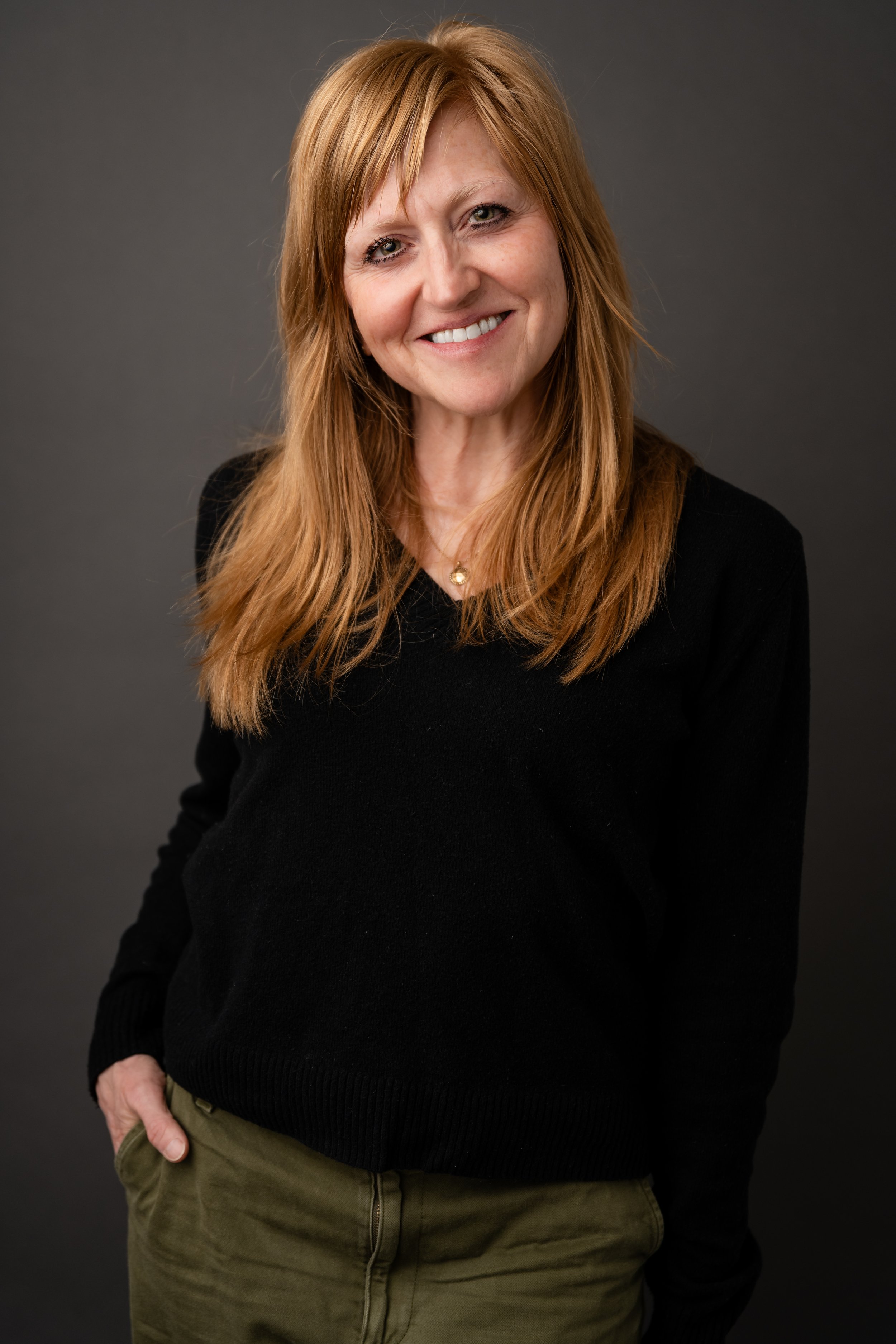 Smiling portrait of a woman wear a black sweater against a gray background