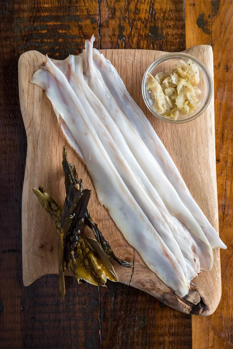 Raw squid with bunashimeji mushrooms, on a wooden cutting board.