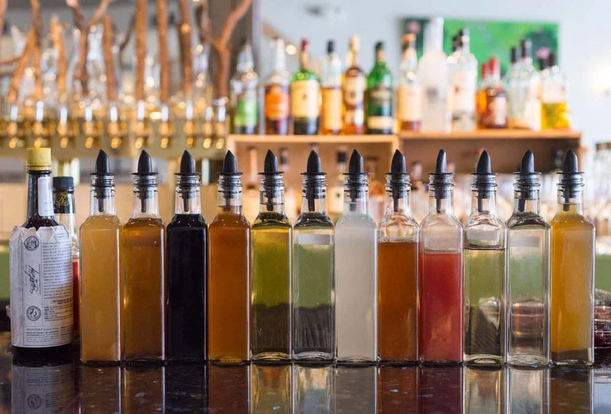 A row of glass bottles filled with colorful liquids, used for cocktails or flavorings, with dropper caps, on a bar counter.