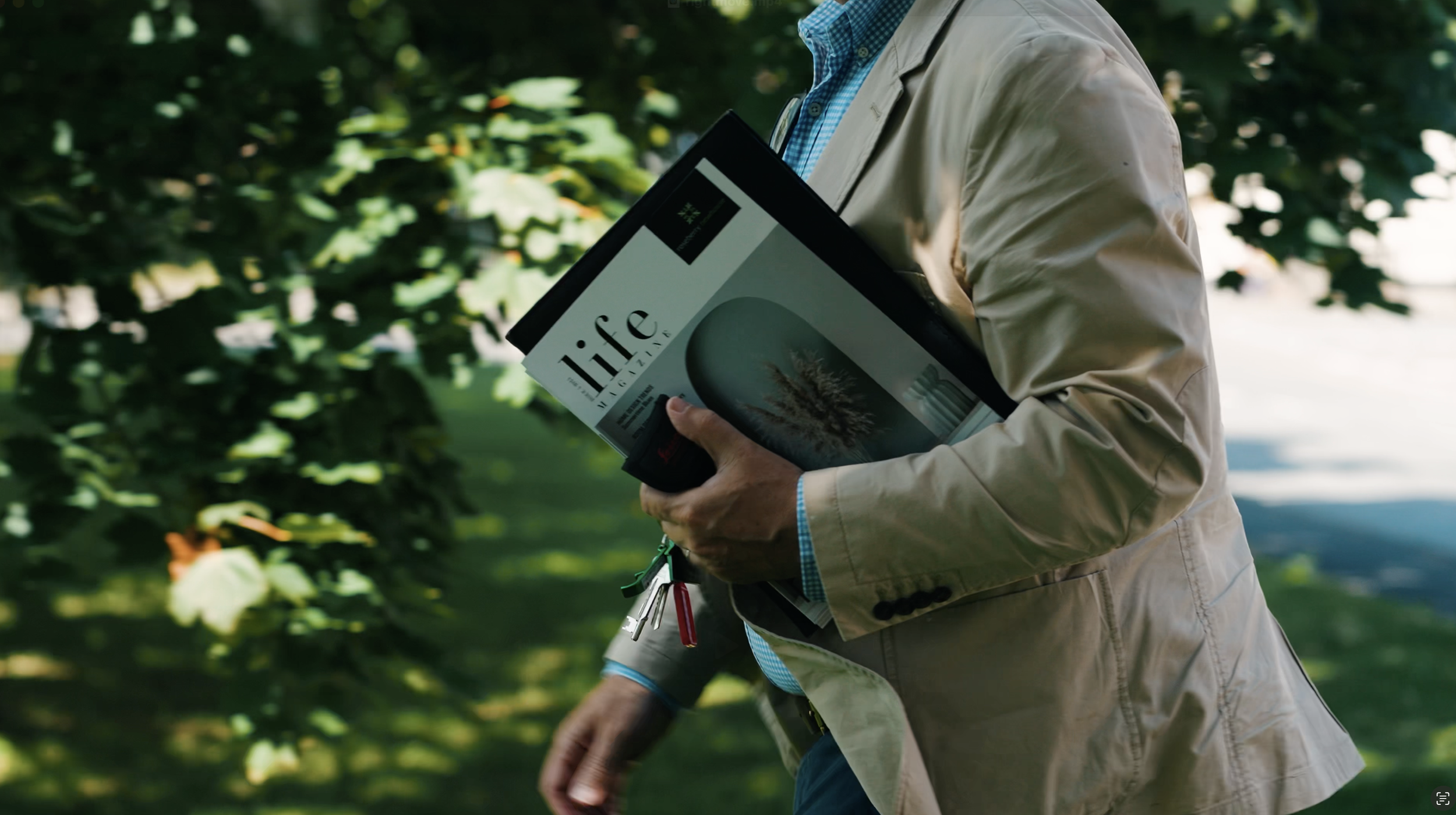 Person walking outdoors in a park or garden, holding a magazine titled 'life magazine' with an image of a tree on the cover.