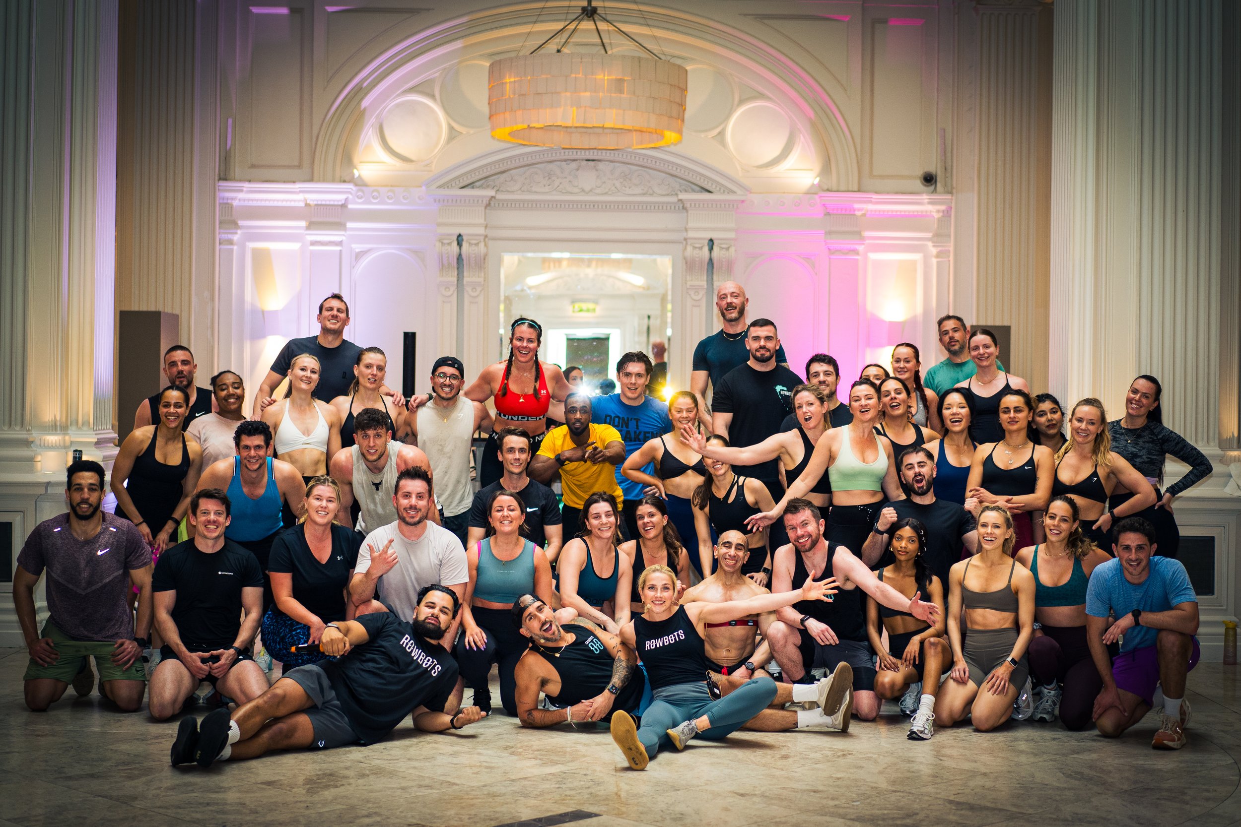 Group of people in athletic wear celebrating indoors in a large, elegant room with ornate ceiling and soft lighting.