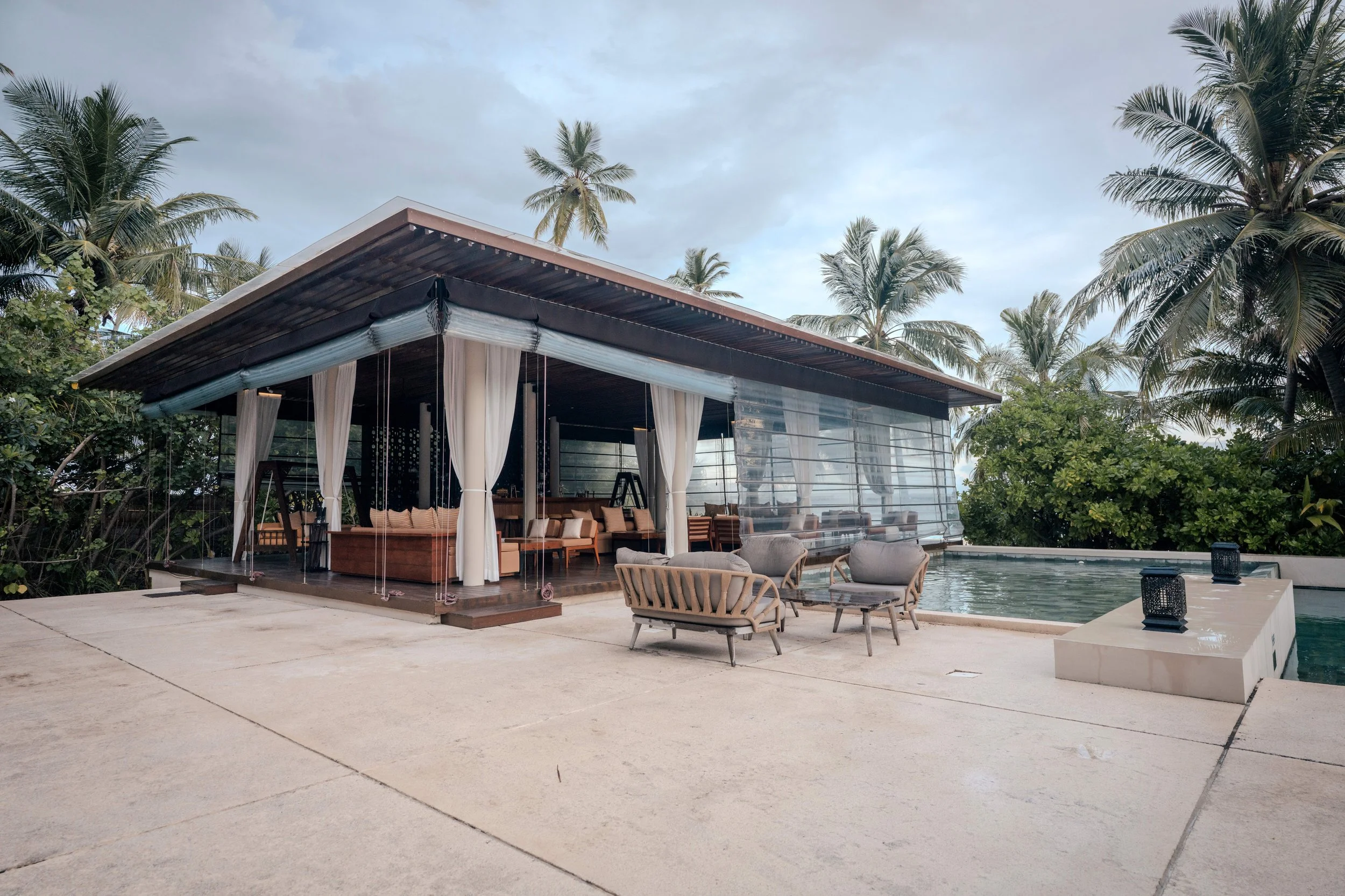 Luxury poolside lounge area with outdoor seating, a small pool, and palm trees in a tropical setting.