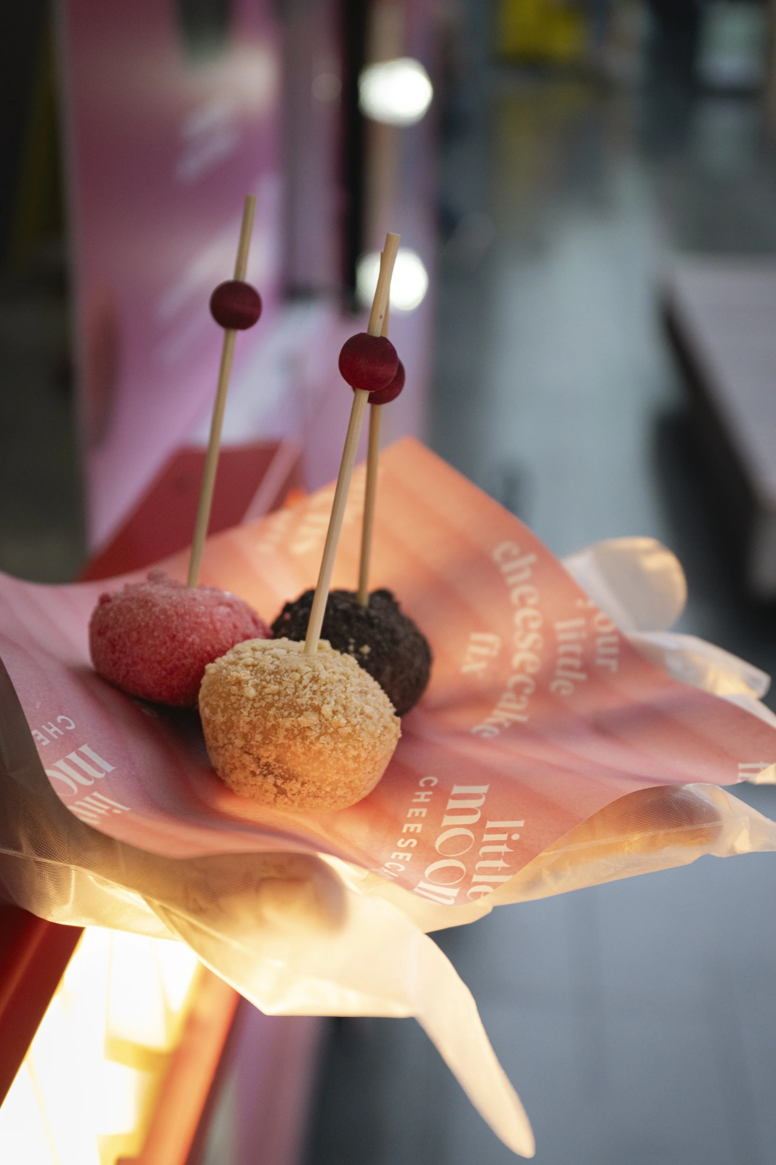 Assorted heart-shaped cheese balls on skewers, displayed on pink paper in a stand.