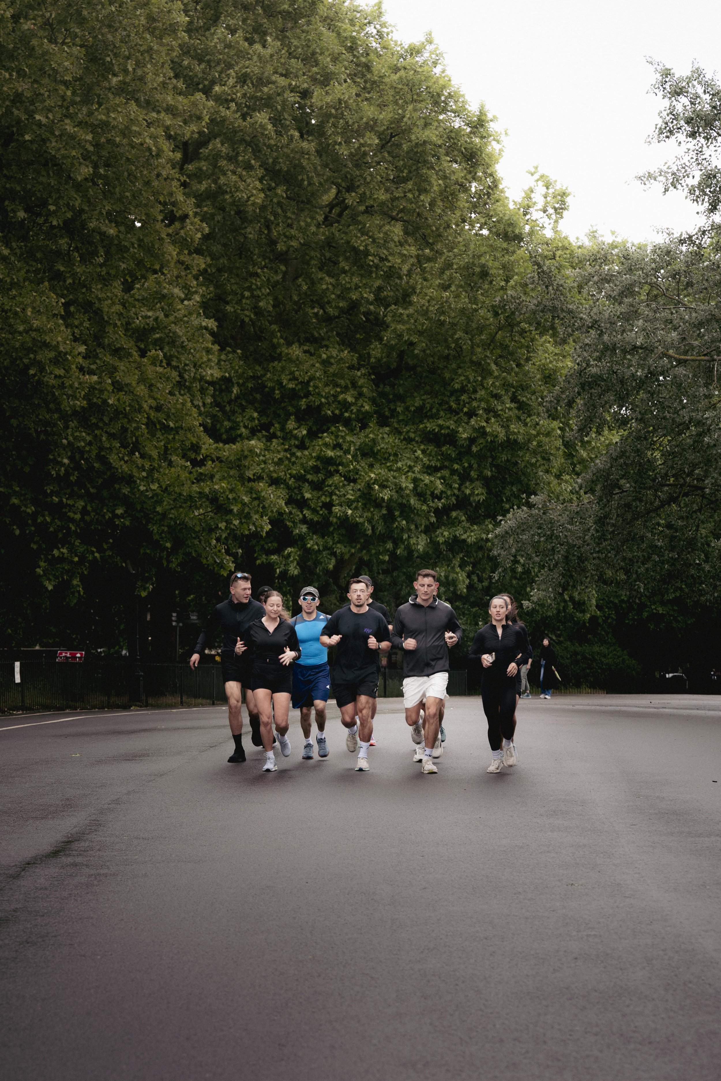 Group of people jogging together on a paved road surrounded by trees.