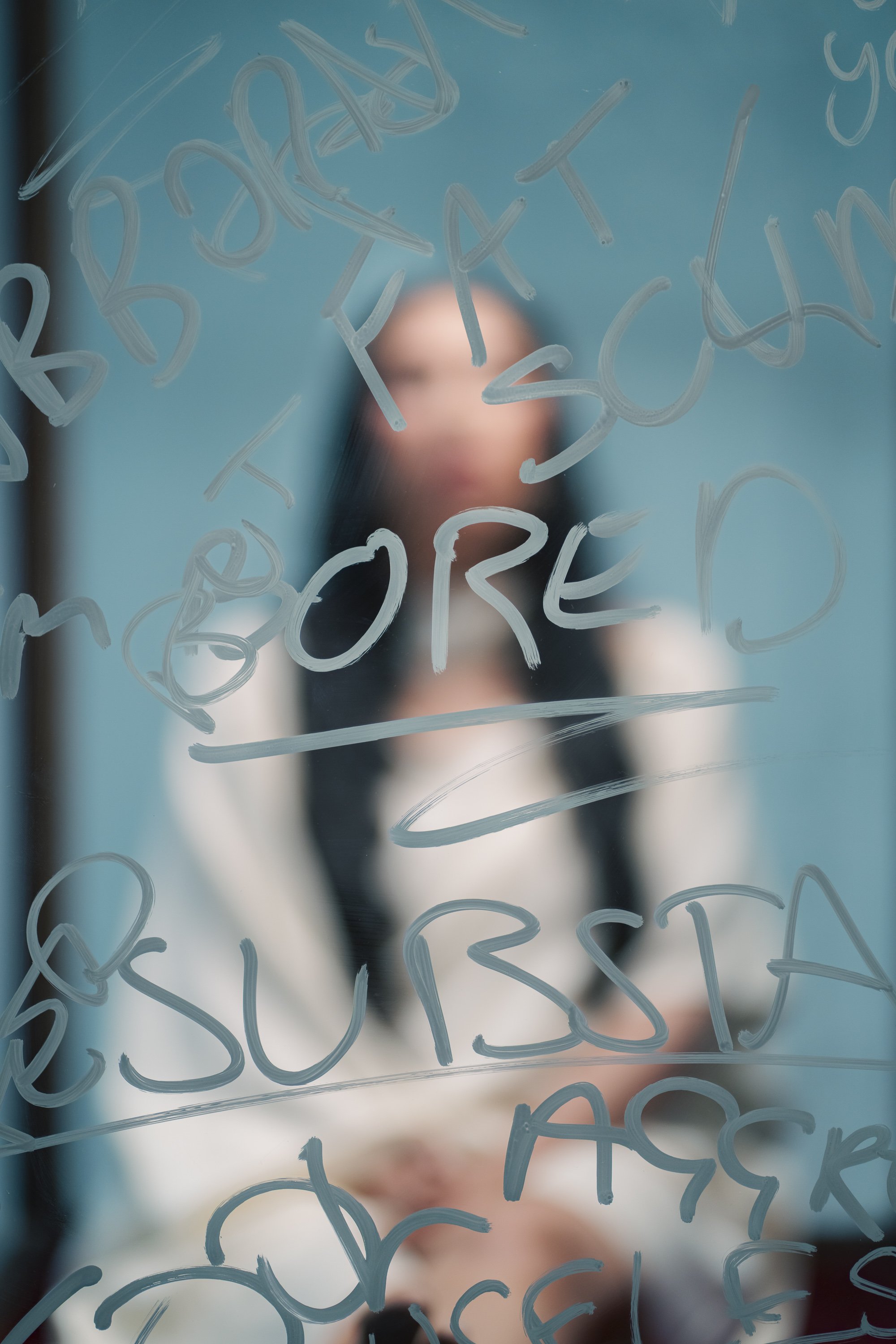 Blurred person writing words on glass with marker, words include 'BOOK', 'BREAD', 'SOUP', and 'PASTA'.