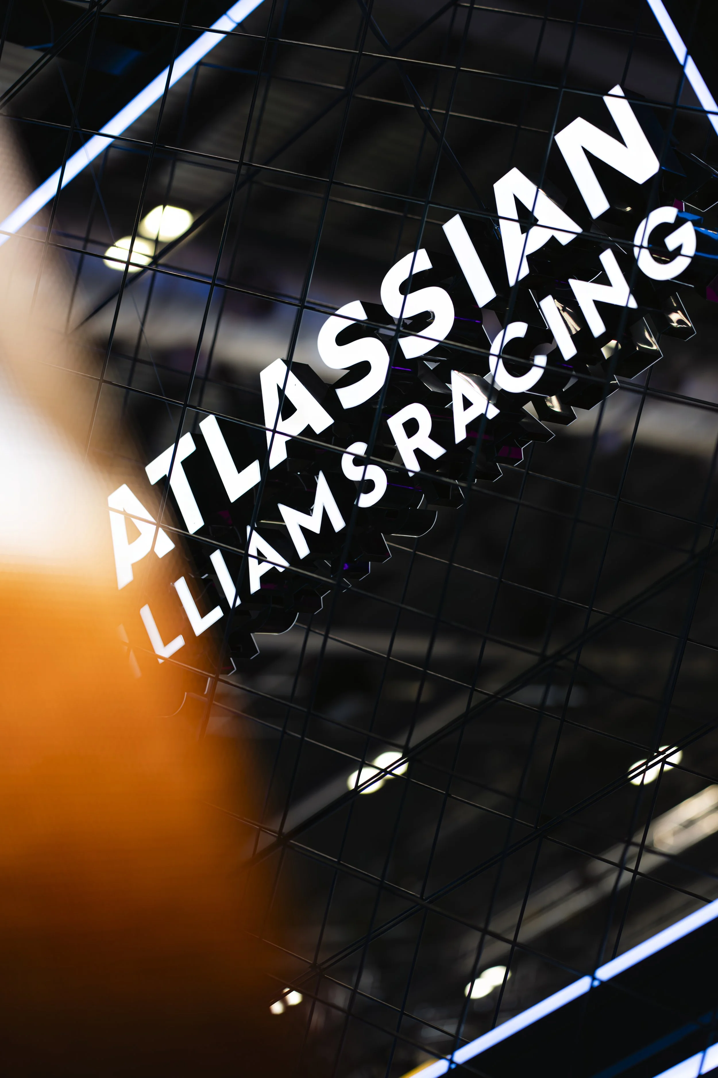 Neon sign displaying the name 'Atlas Asian Liams Racing' behind a wire grid at an indoor event or exhibition.
