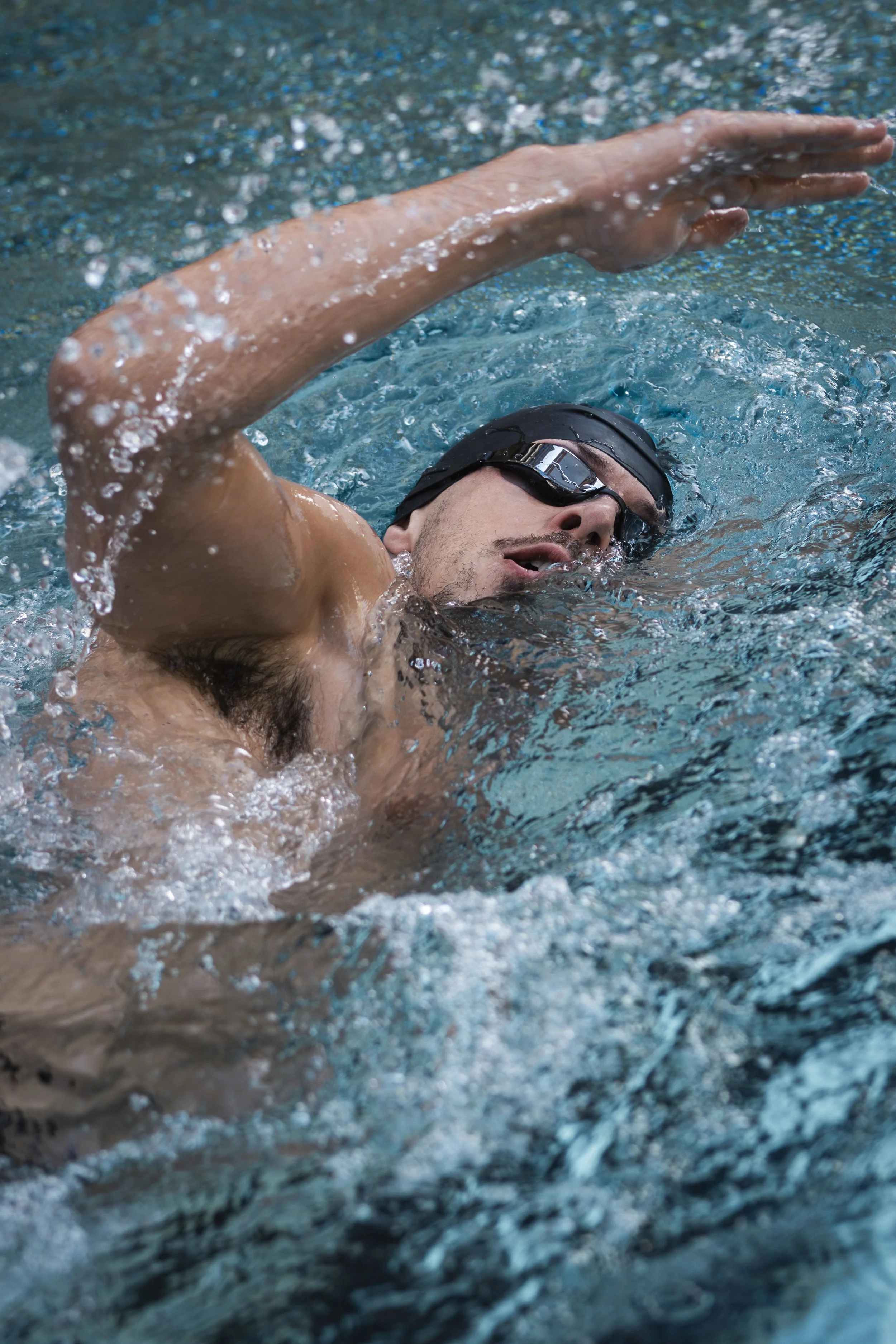 A male swimmer with goggles practicing freestyle stroke in a swimming pool.