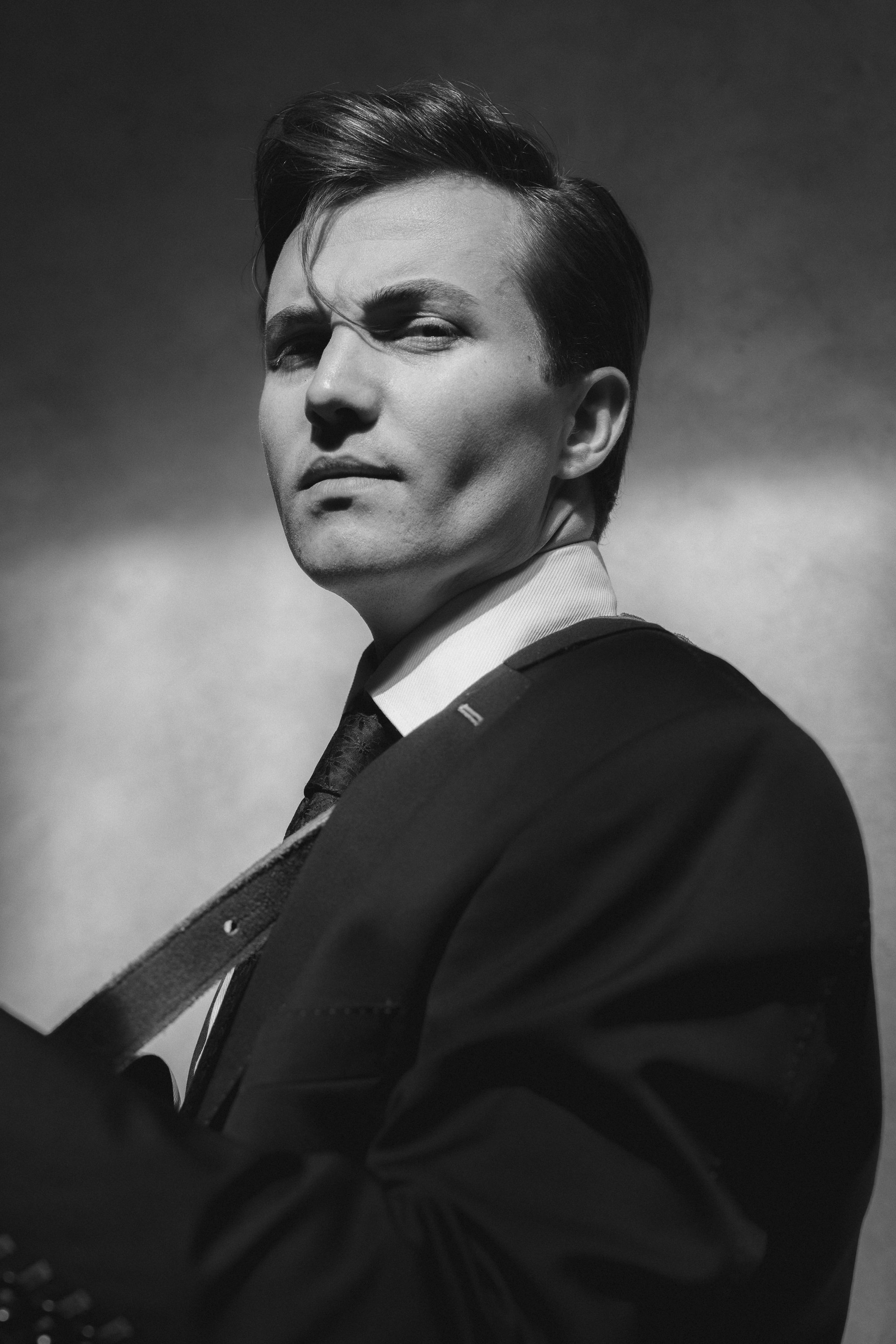 Black and white photo of a man in a suit holding a guitar, with a serious expression, against a plain background.