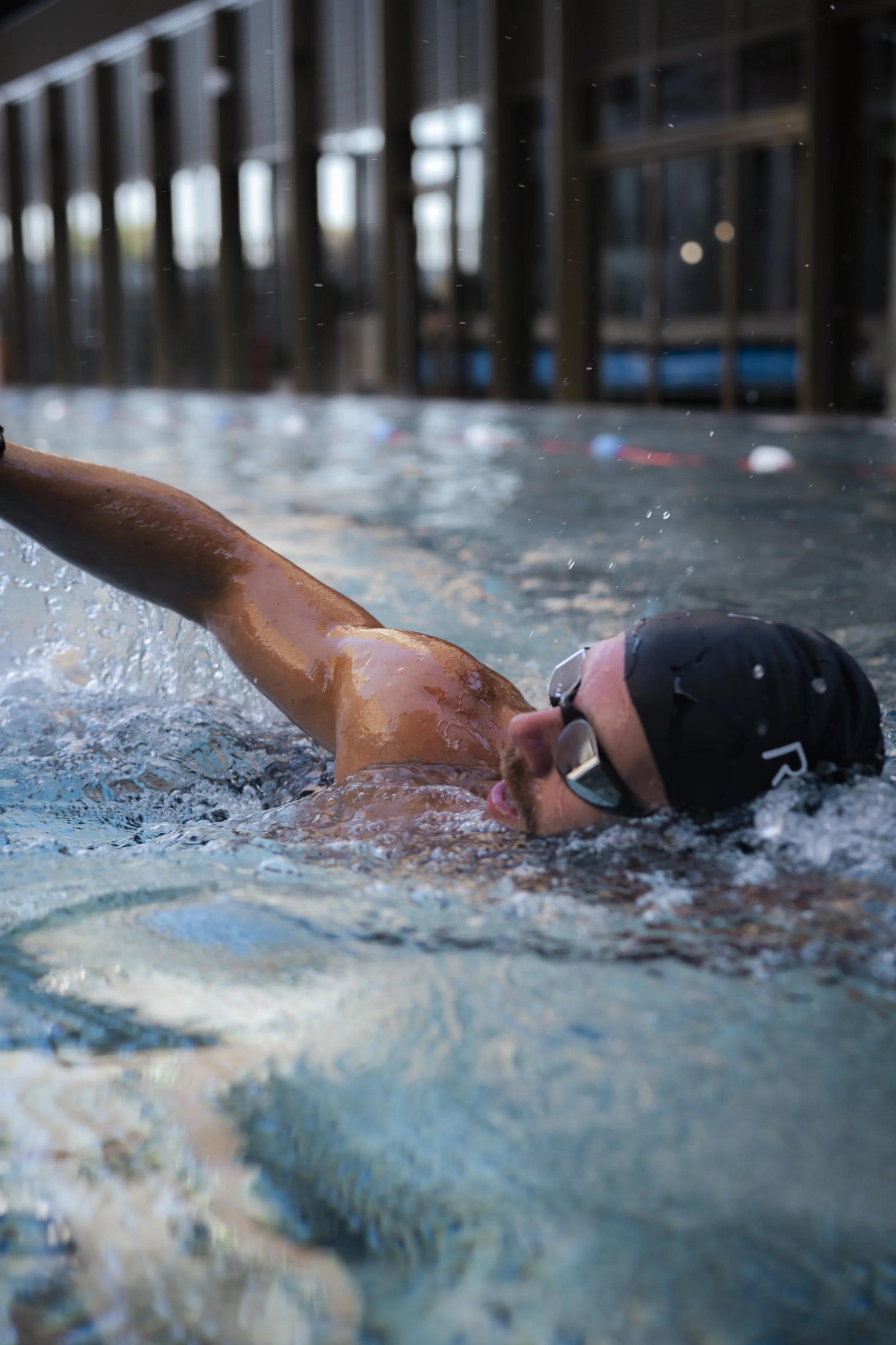 A man swimming in an indoor pool wearing goggles, a swim cap, and no shirt.