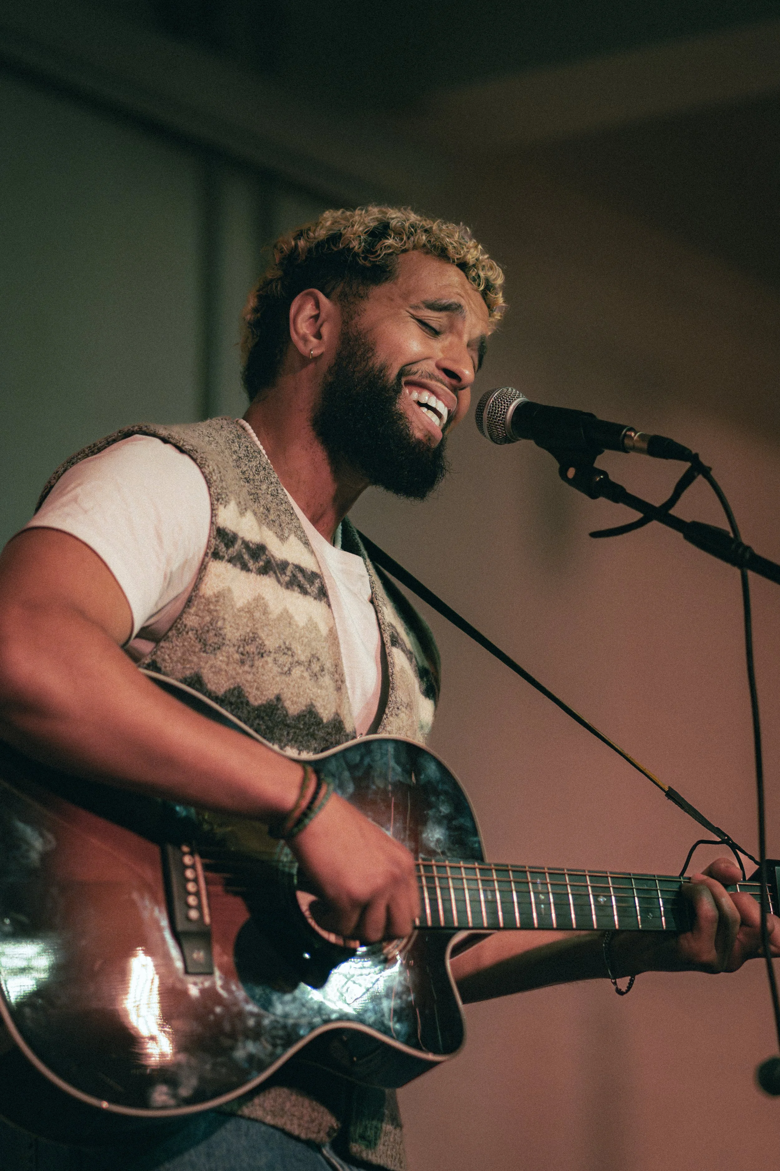 A male musician passionately singing and playing an acoustic guitar on stage.