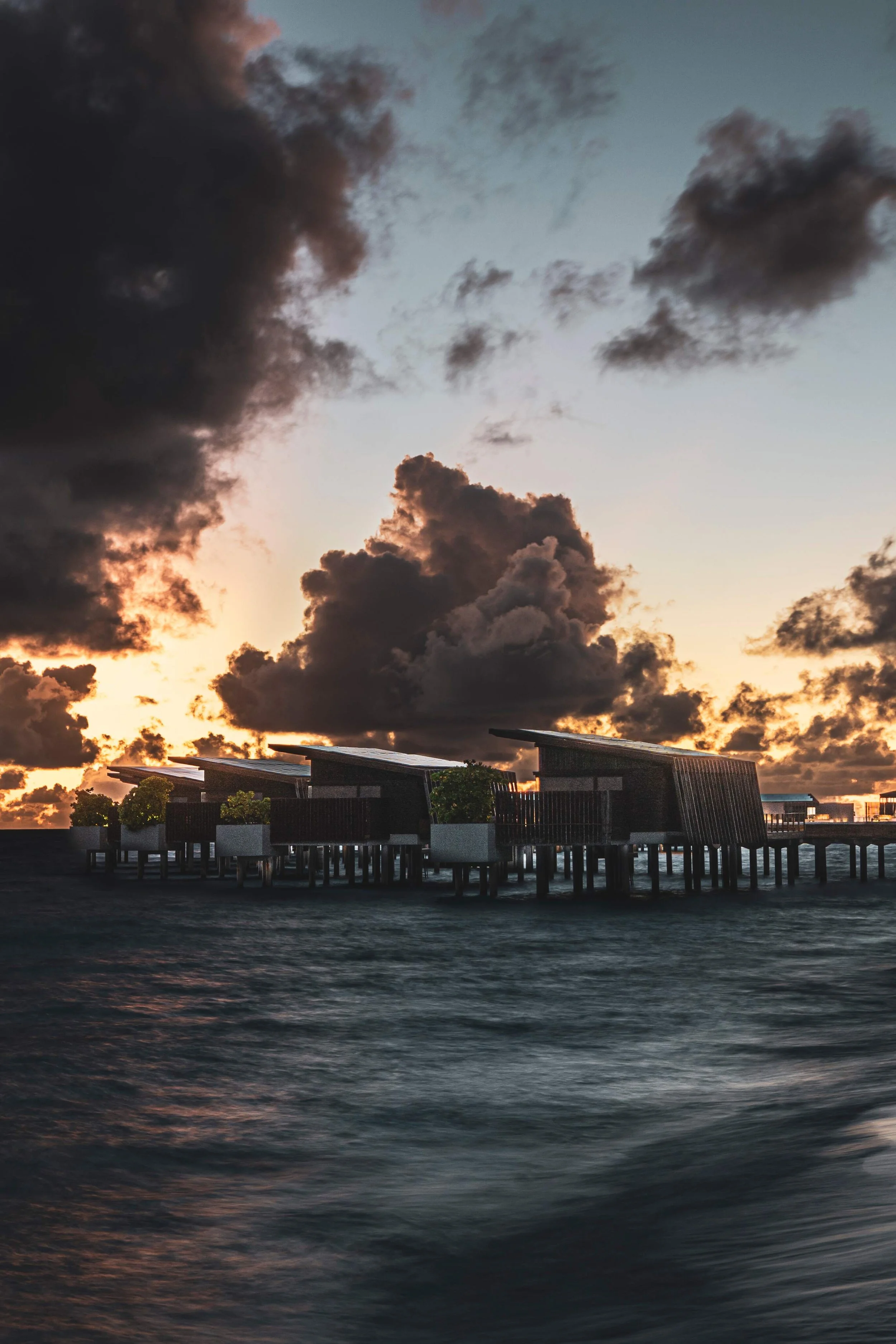 Overwater bungalows at sunset with dark clouds in the sky.