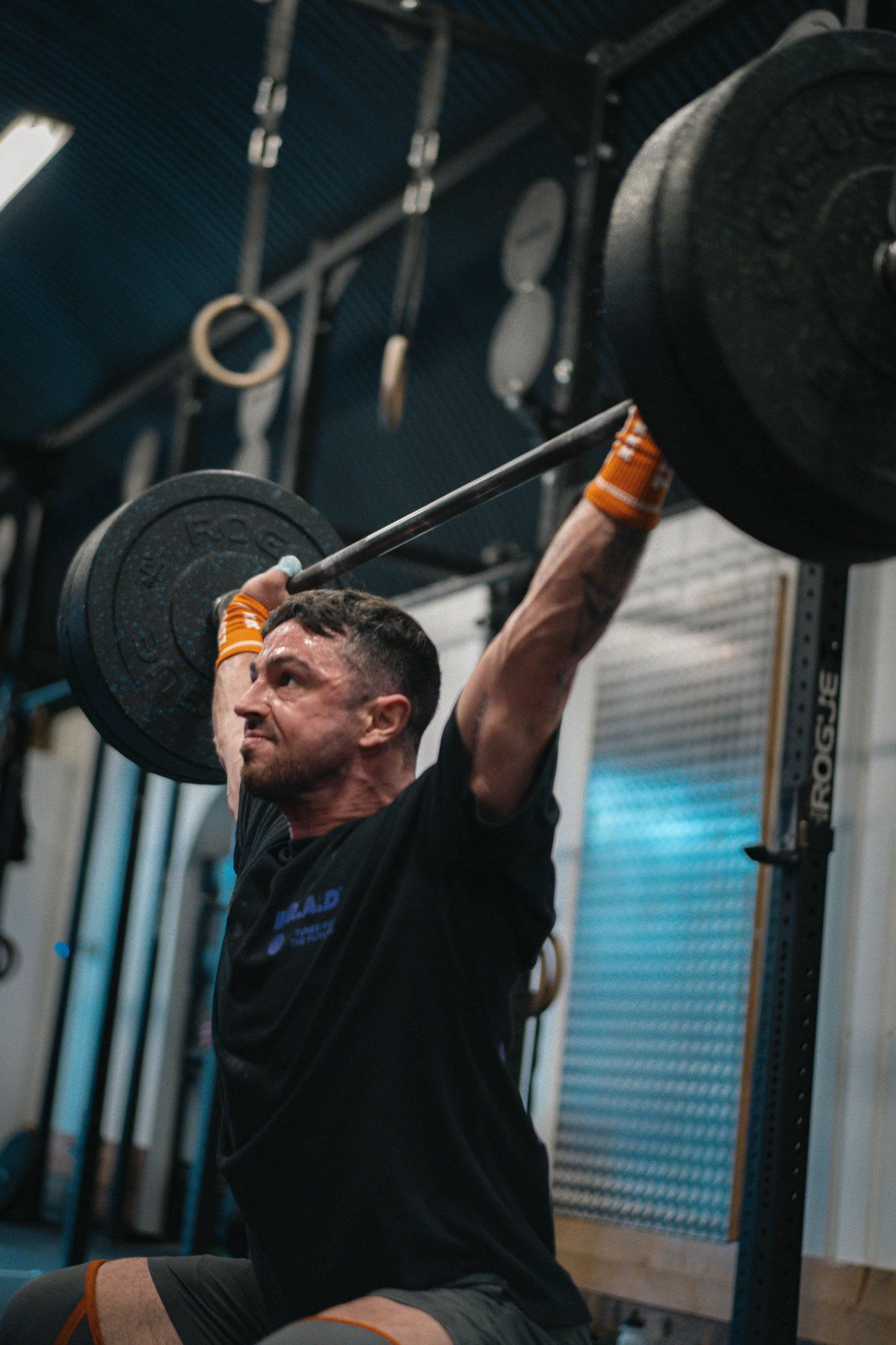 Man lifting a barbell with weights overhead in a gym.