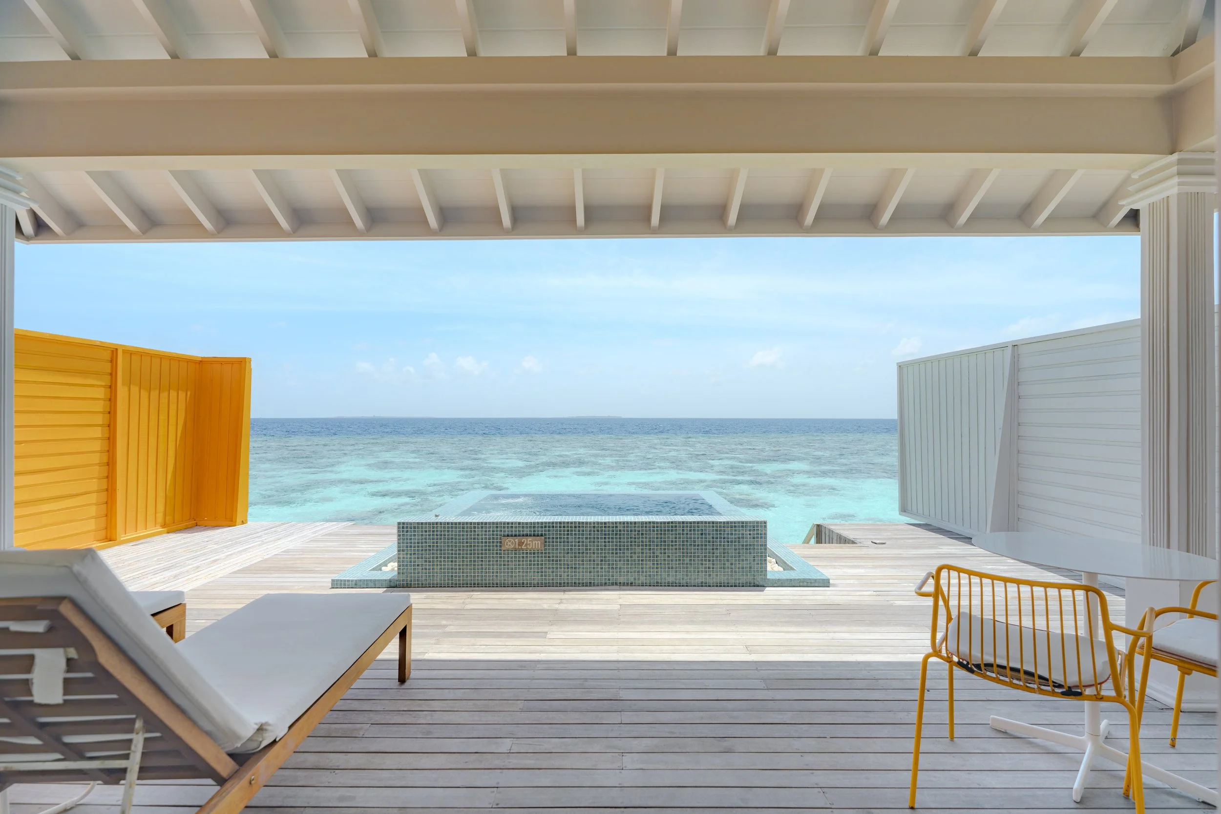 View of the ocean from a shaded deck with lounge chairs, a small pool, and colorful privacy fences.