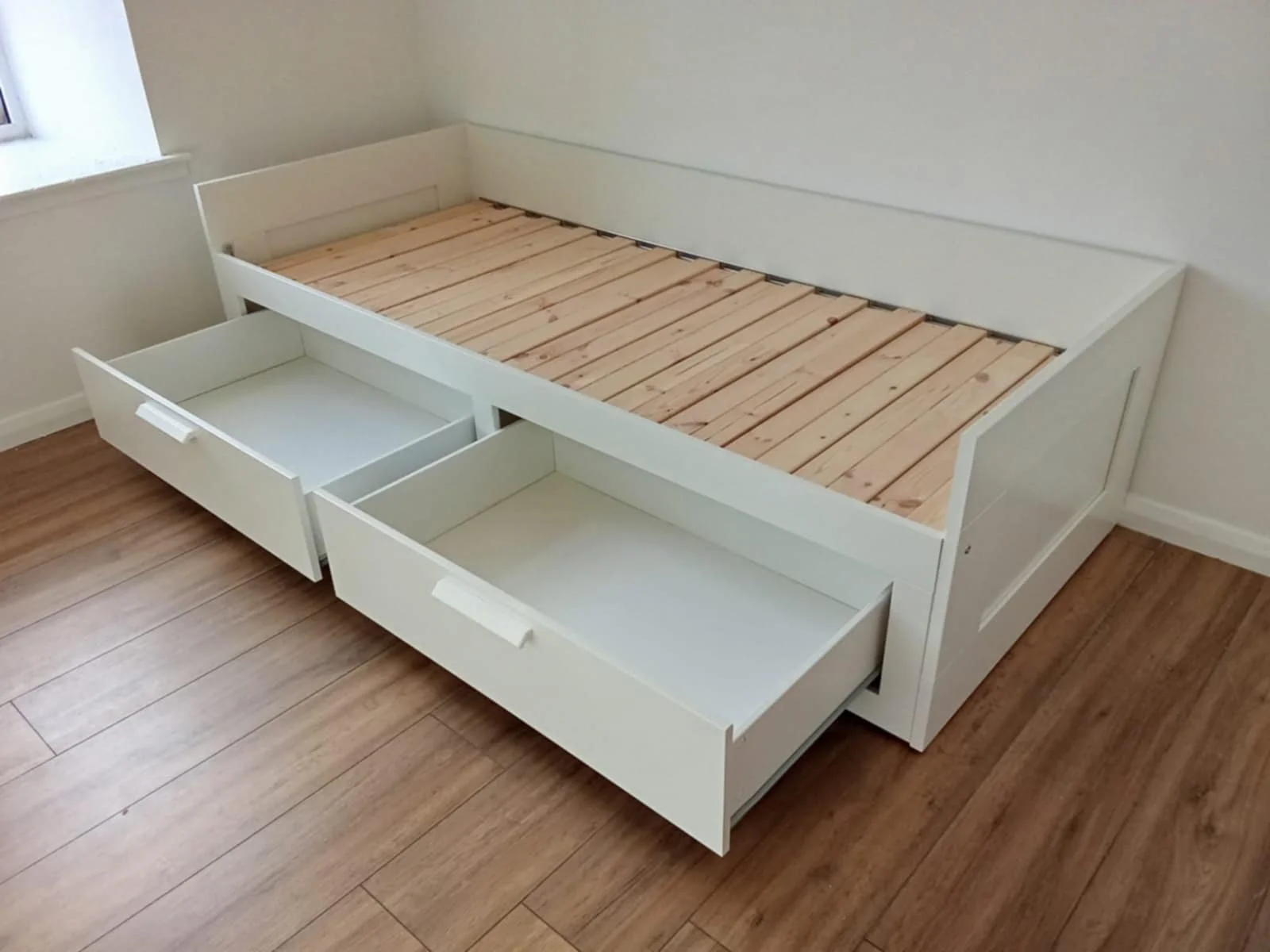 A blueprint of a cabinet or wardrobe with hardware parts scattered on top, including screws, wooden dowels, and brackets.