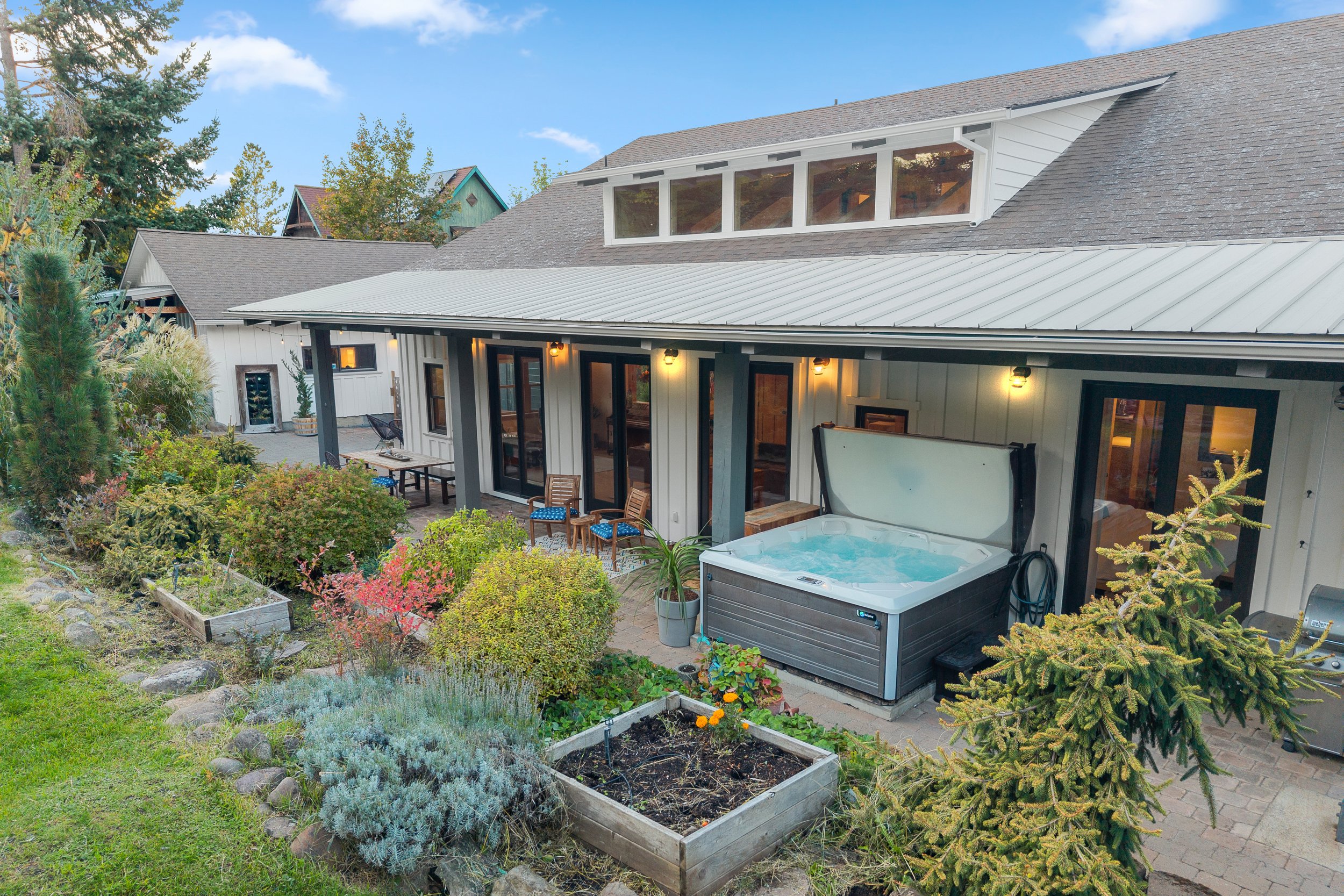 Backyard patio of a house with lounge chairs, hot tub, and garden with potted plants and flowers.