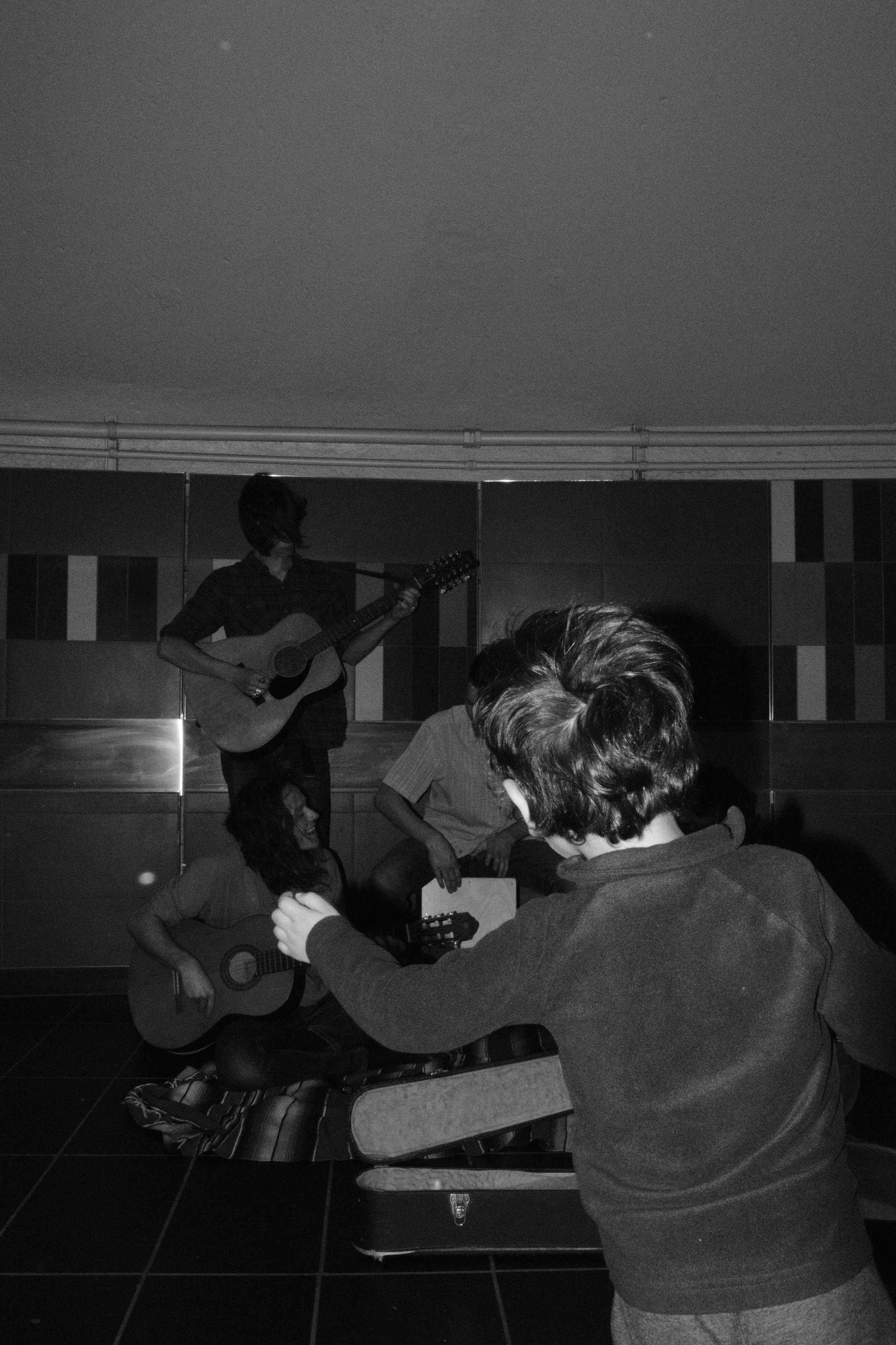A group of young people playing guitars and singing together in a casual setting.