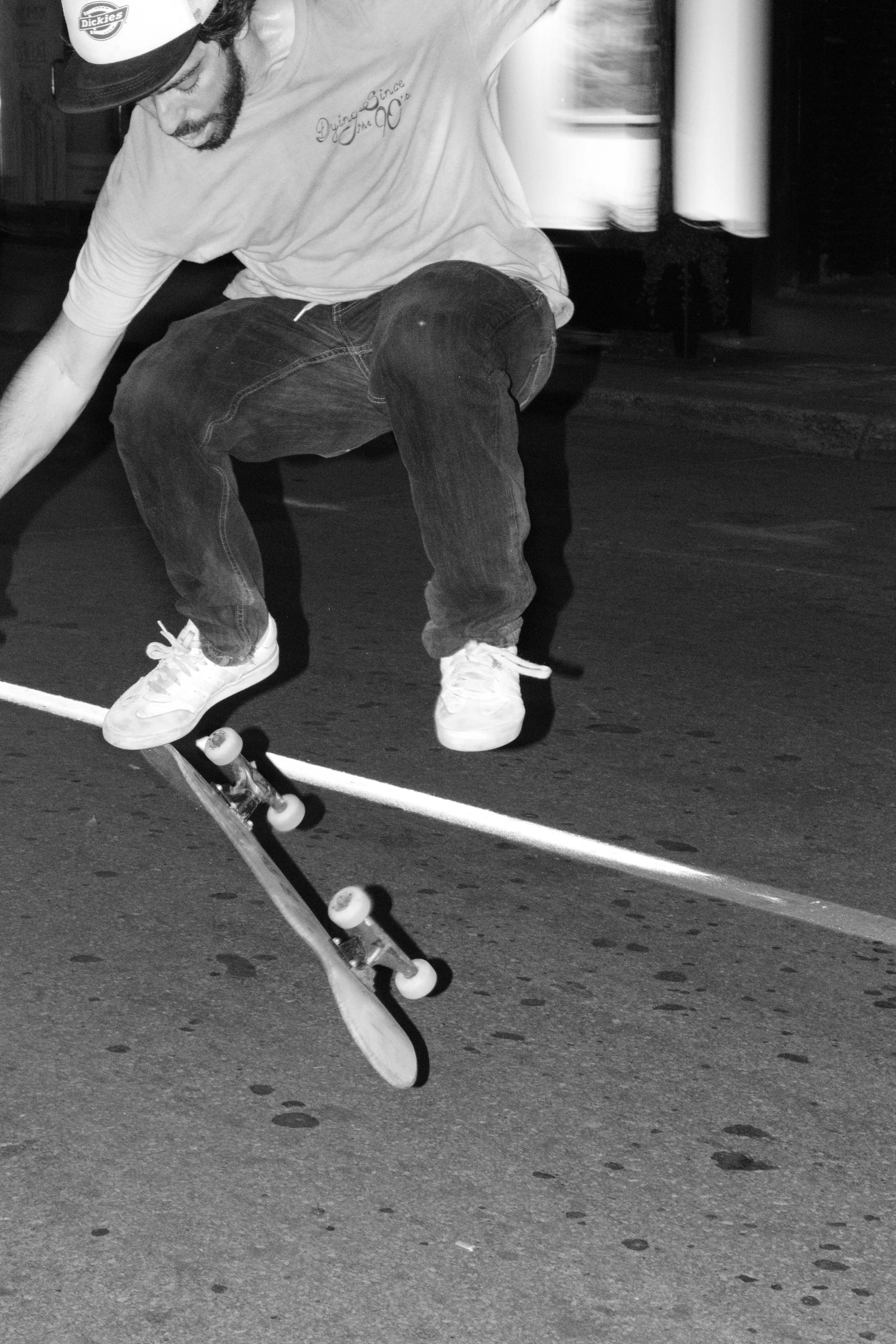 A skateboarder performing an ollie on a street at night, captured in black and white.